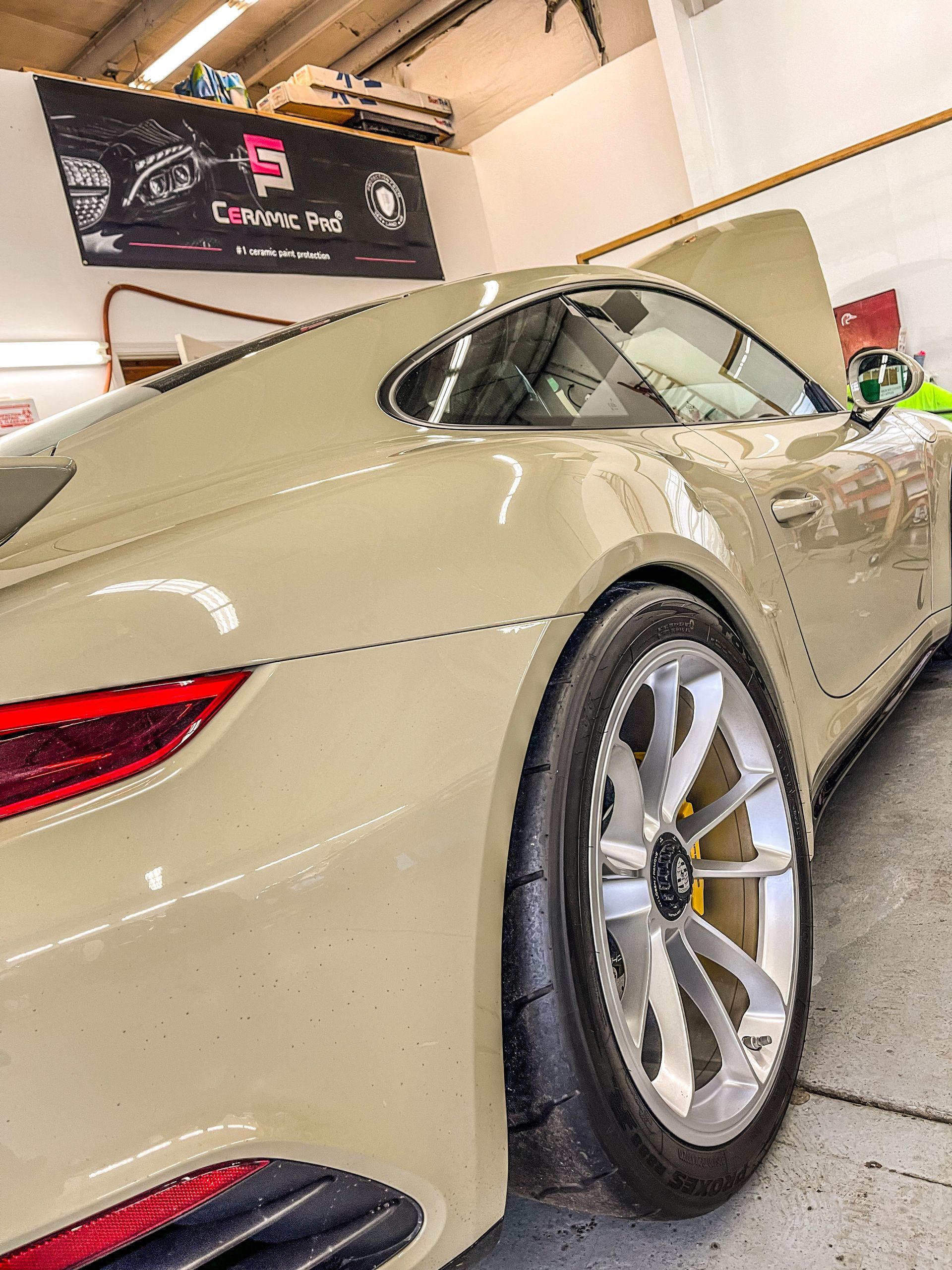 Tan Porsche sports car in a garage with hood open, showing a wheel and taillight.