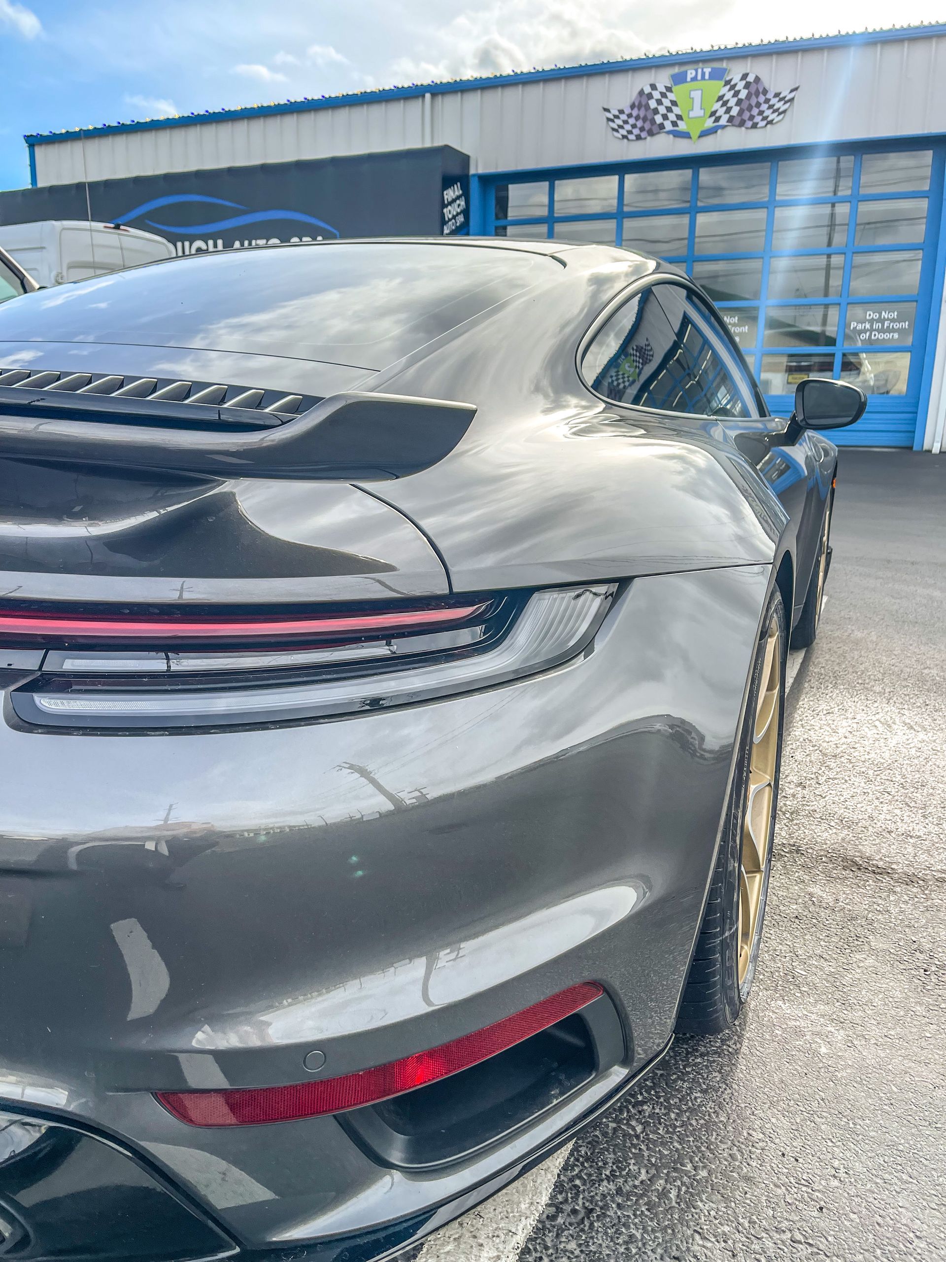Gray Porsche sports car parked outside a building, sunny day.