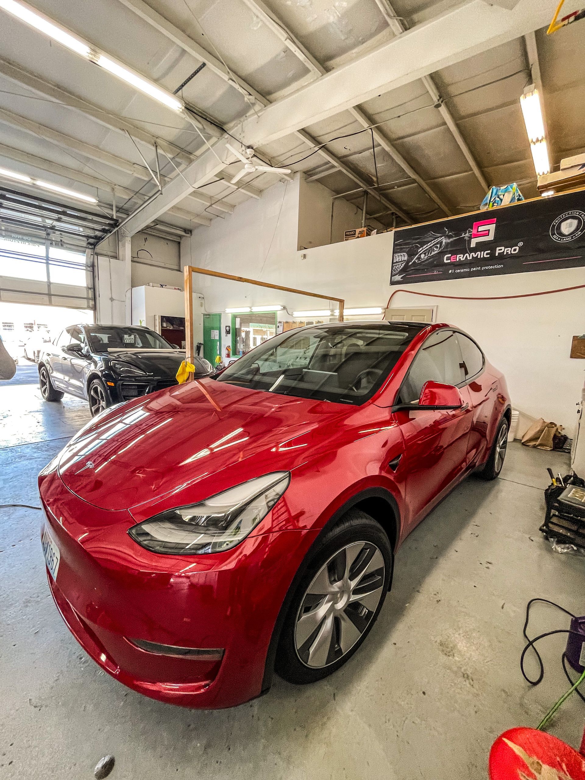 Red Tesla Model Y inside a garage. Another black car in the background. Overhead lighting.