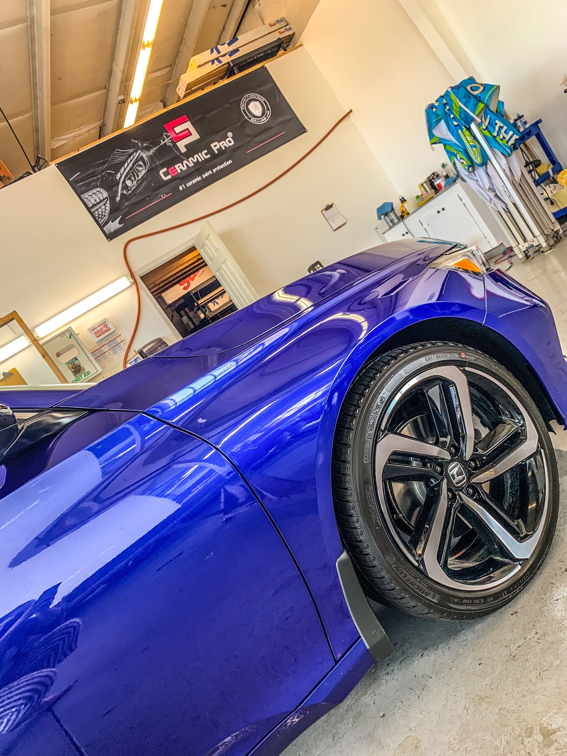 Blue car in a car detailing shop; a close-up of the front, with shiny tires and a banner in the background.