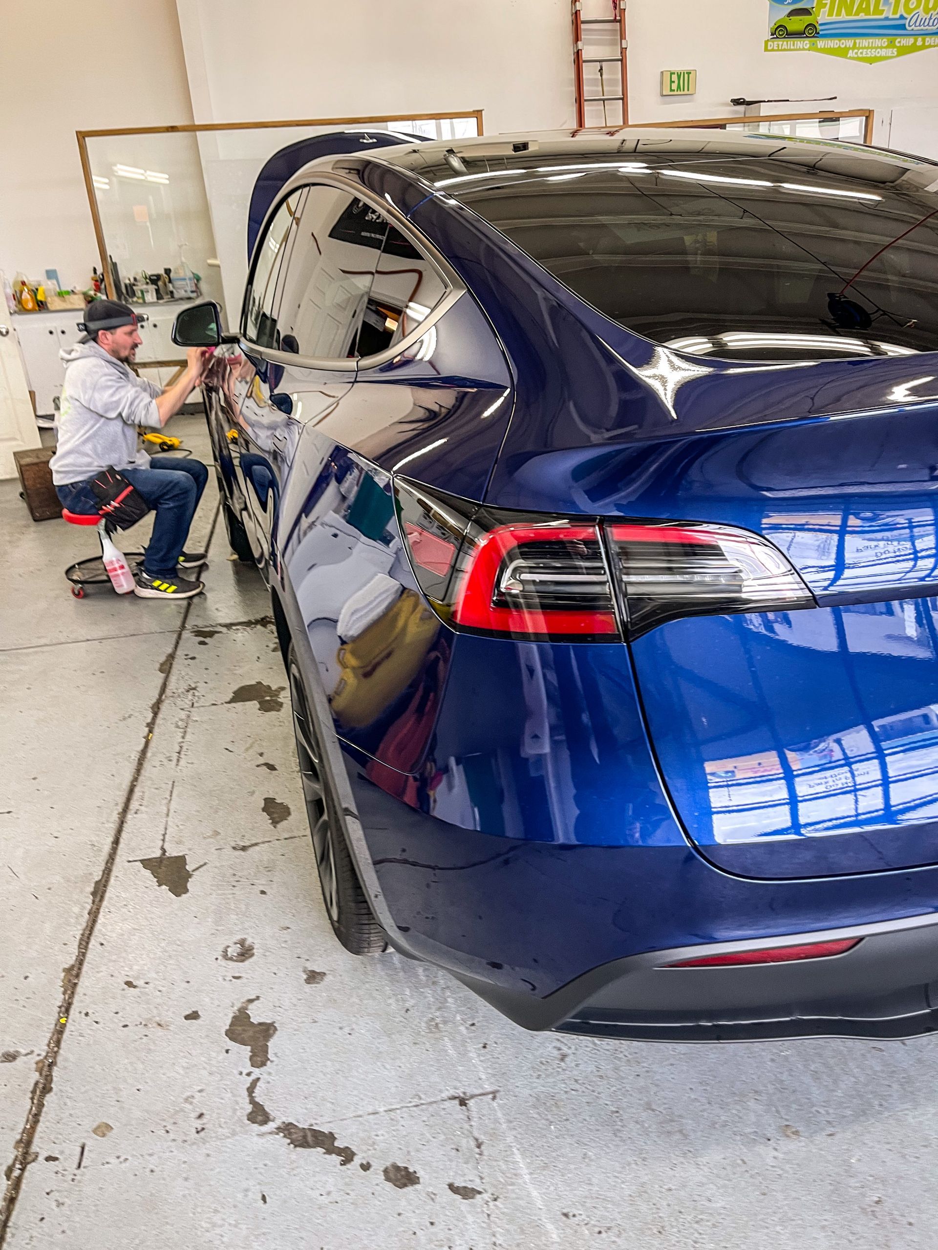 A man applies tint to a blue Tesla car window inside a garage.