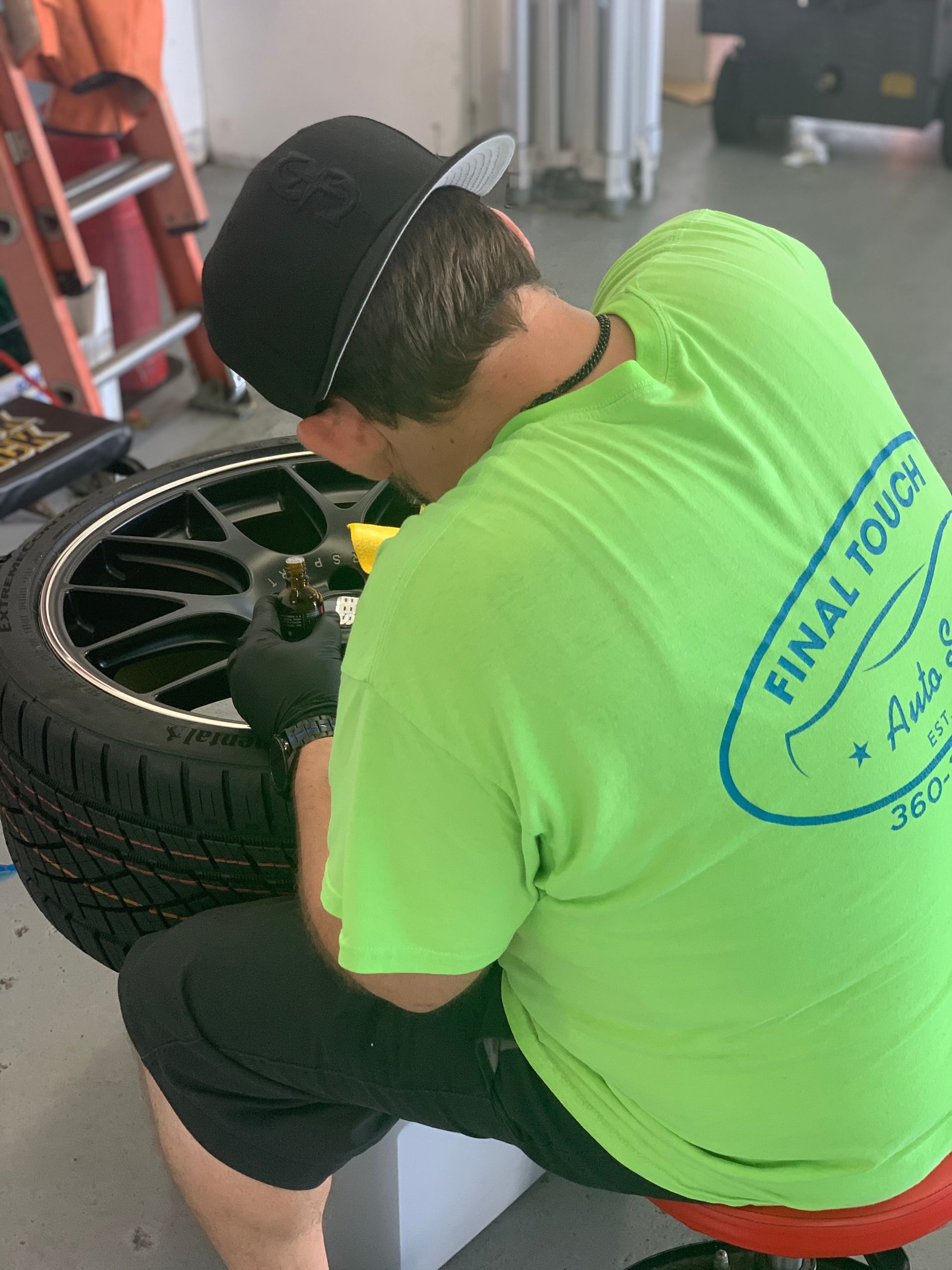 Person in a green shirt working on a tire. Wearing a hat, in a garage.