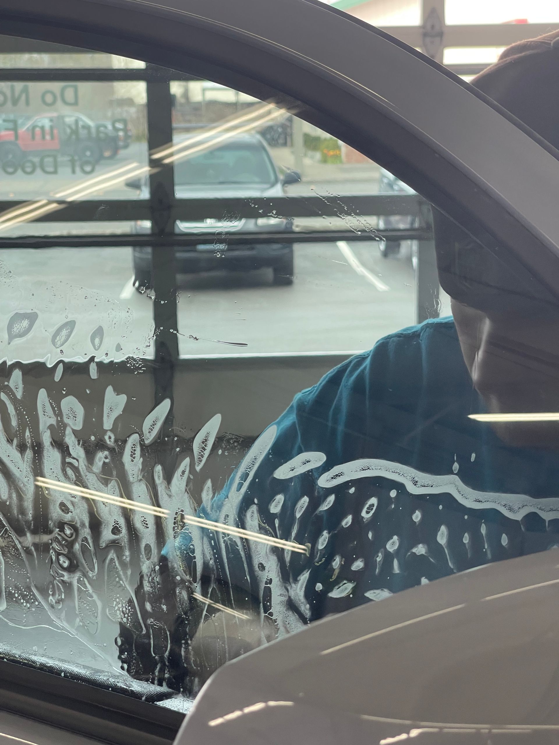 Person washing a car window with soapy water; other cars visible outside.