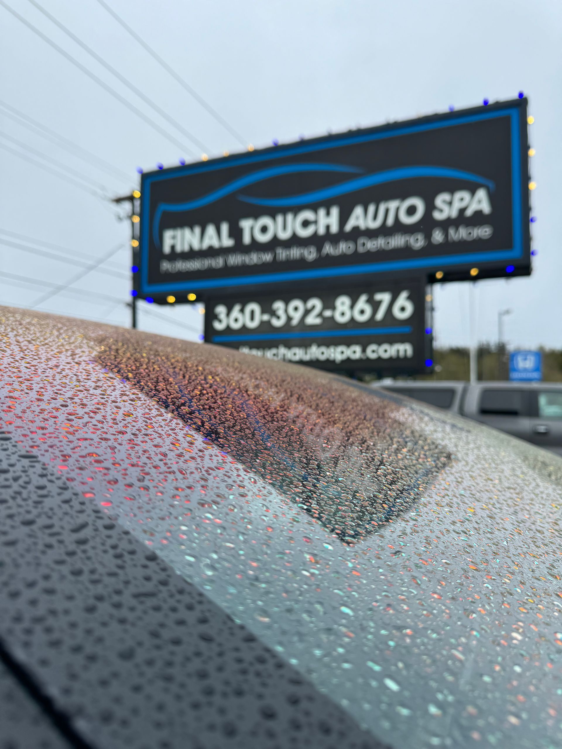 Raindrops on a car windshield with a Final Touch Auto Spa sign in the background.