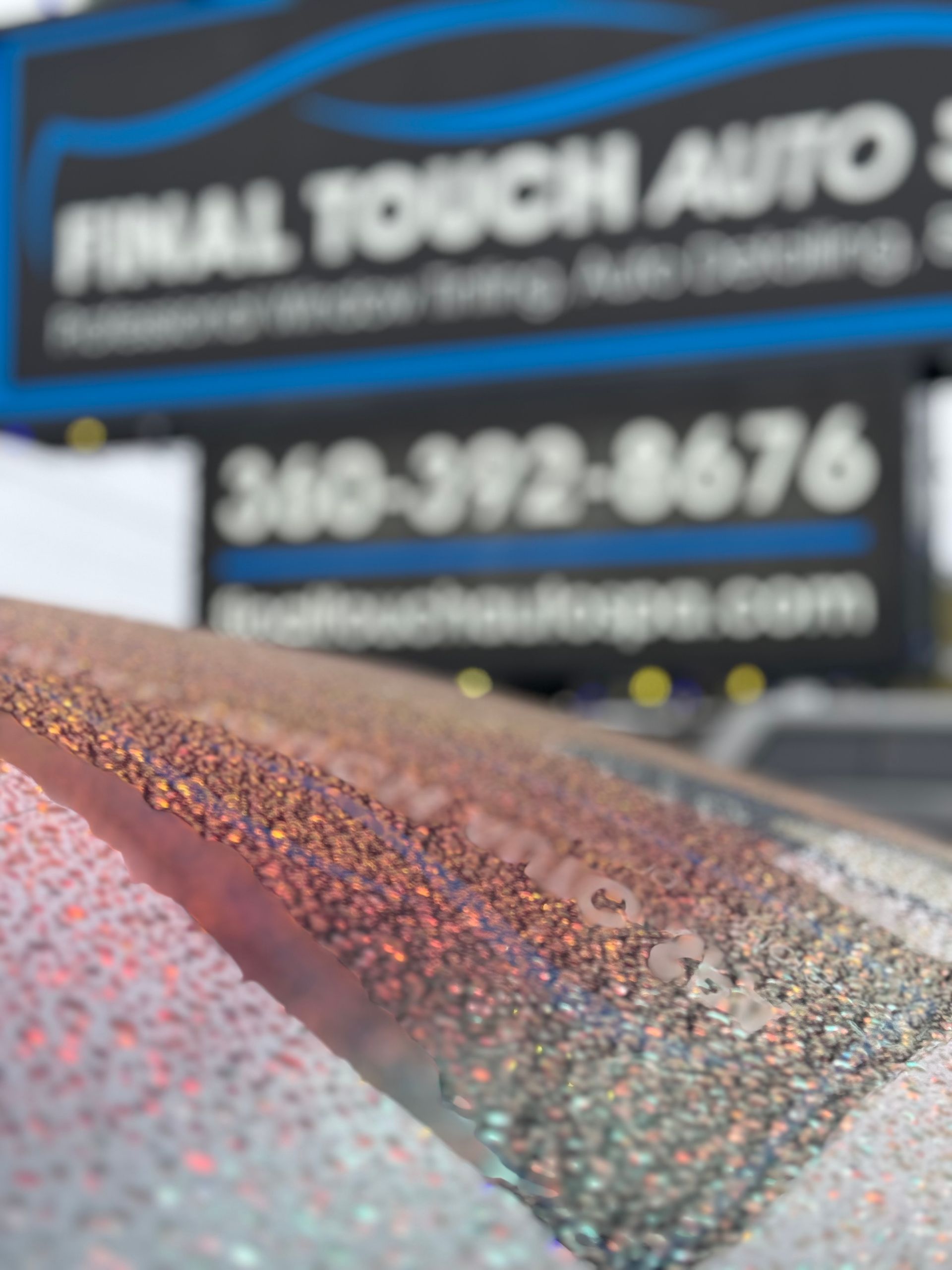 Close-up of a car windshield covered in water droplets with a blurred sign for 