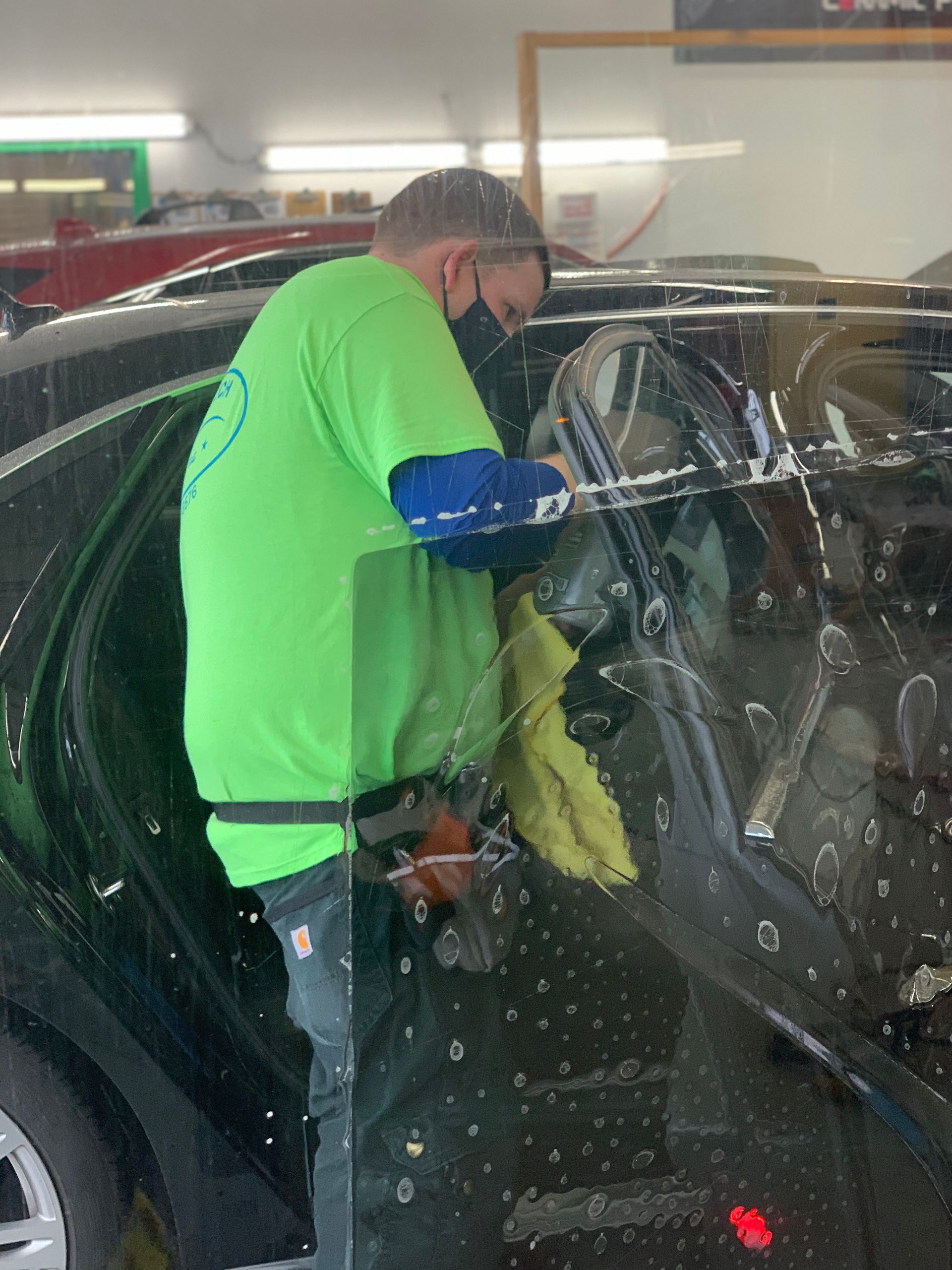 Person in green shirt applying tint to a car window, indoors.