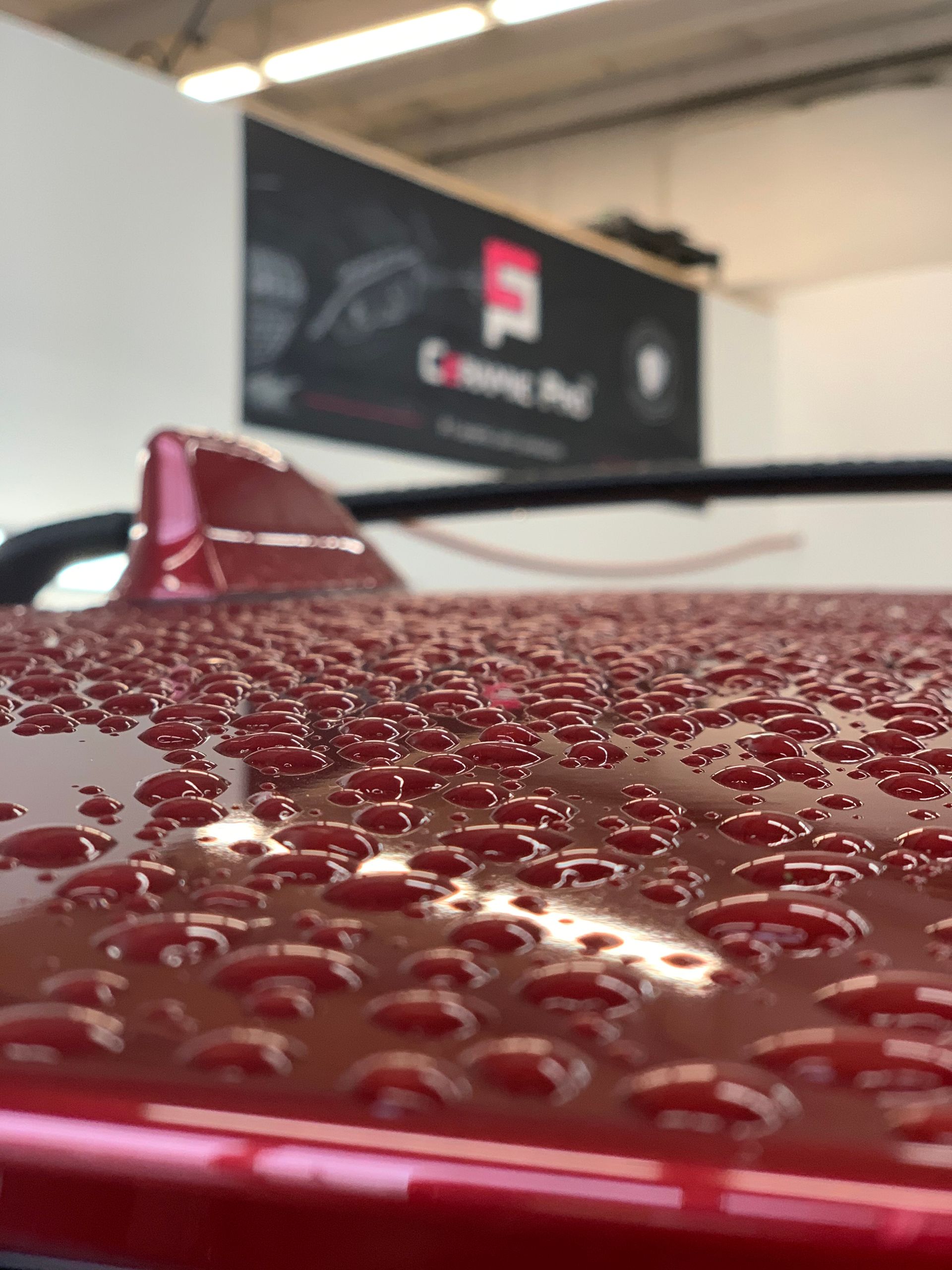 Red car roof covered in water droplets with a fin antenna and a sign in the background.