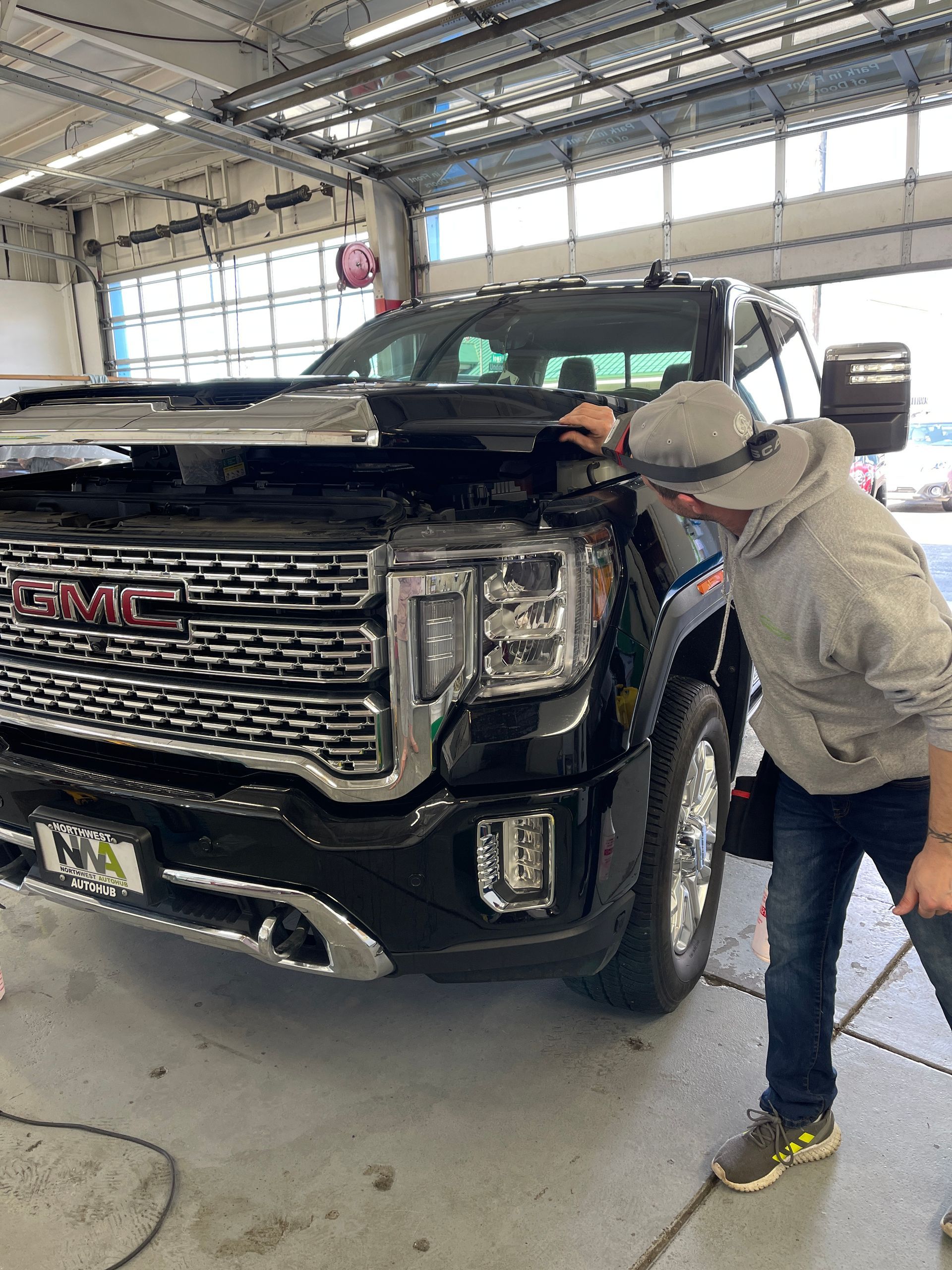 A person inspecting the hood of a black GMC truck inside a garage.