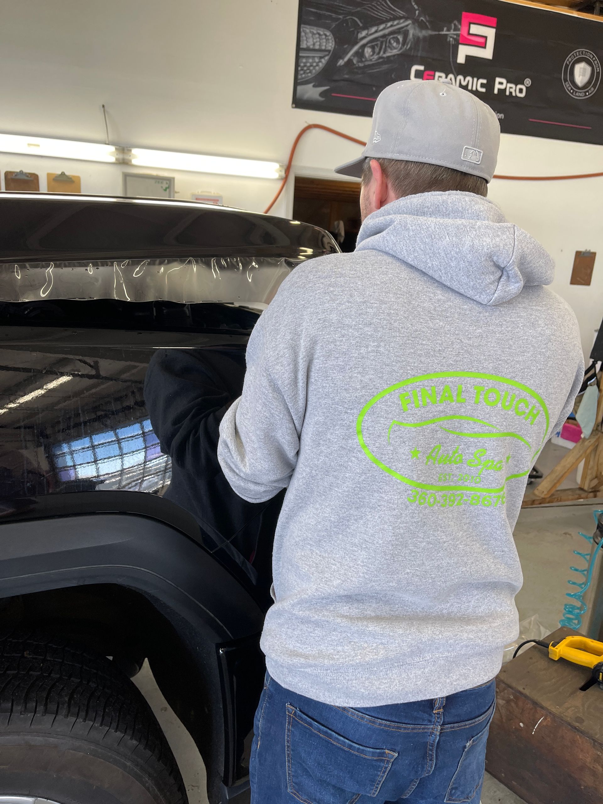 Man in grey hoodie applying film to a vehicle window in a garage.