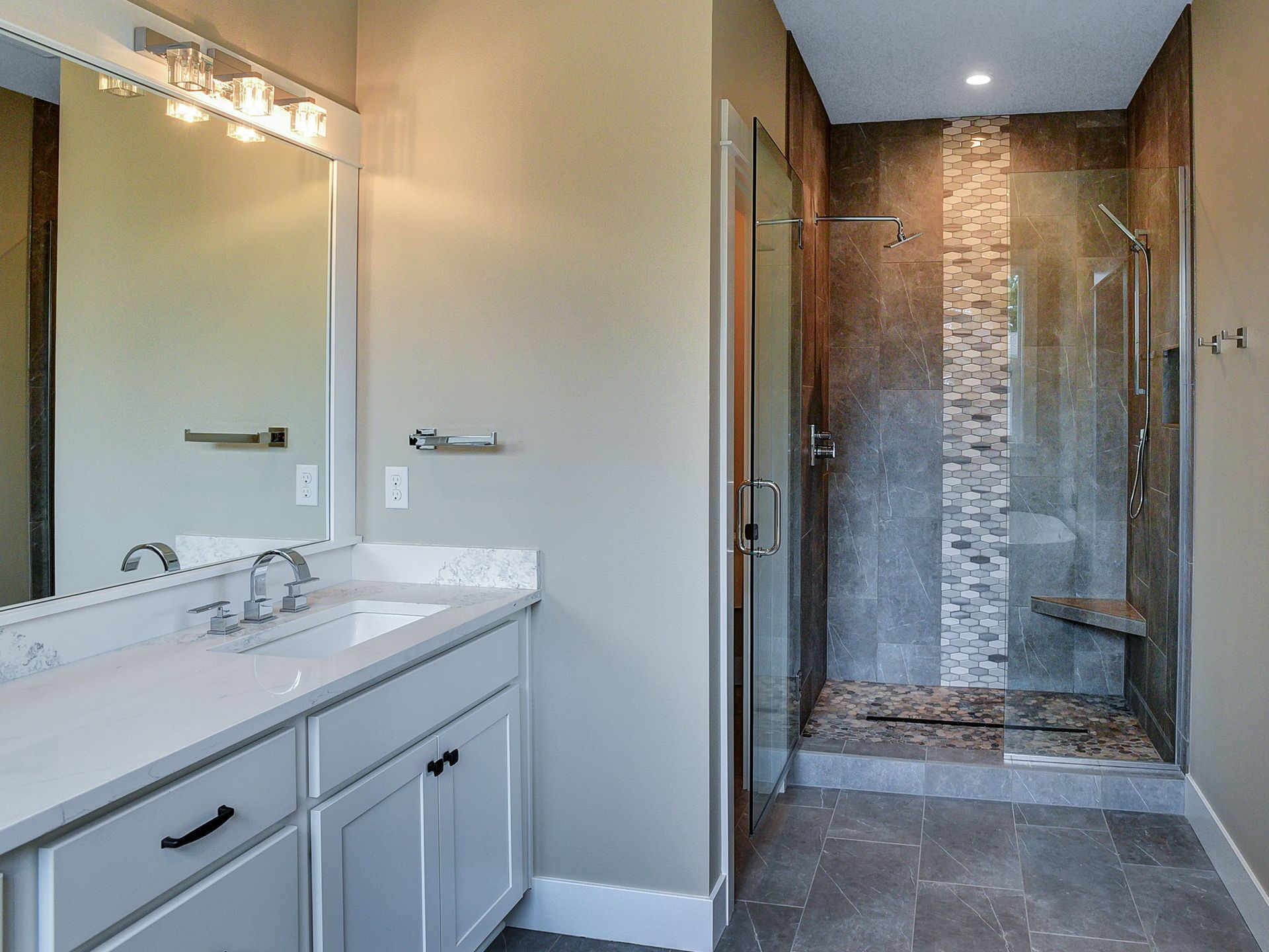 A bathroom with a sink , mirror and walk in shower.