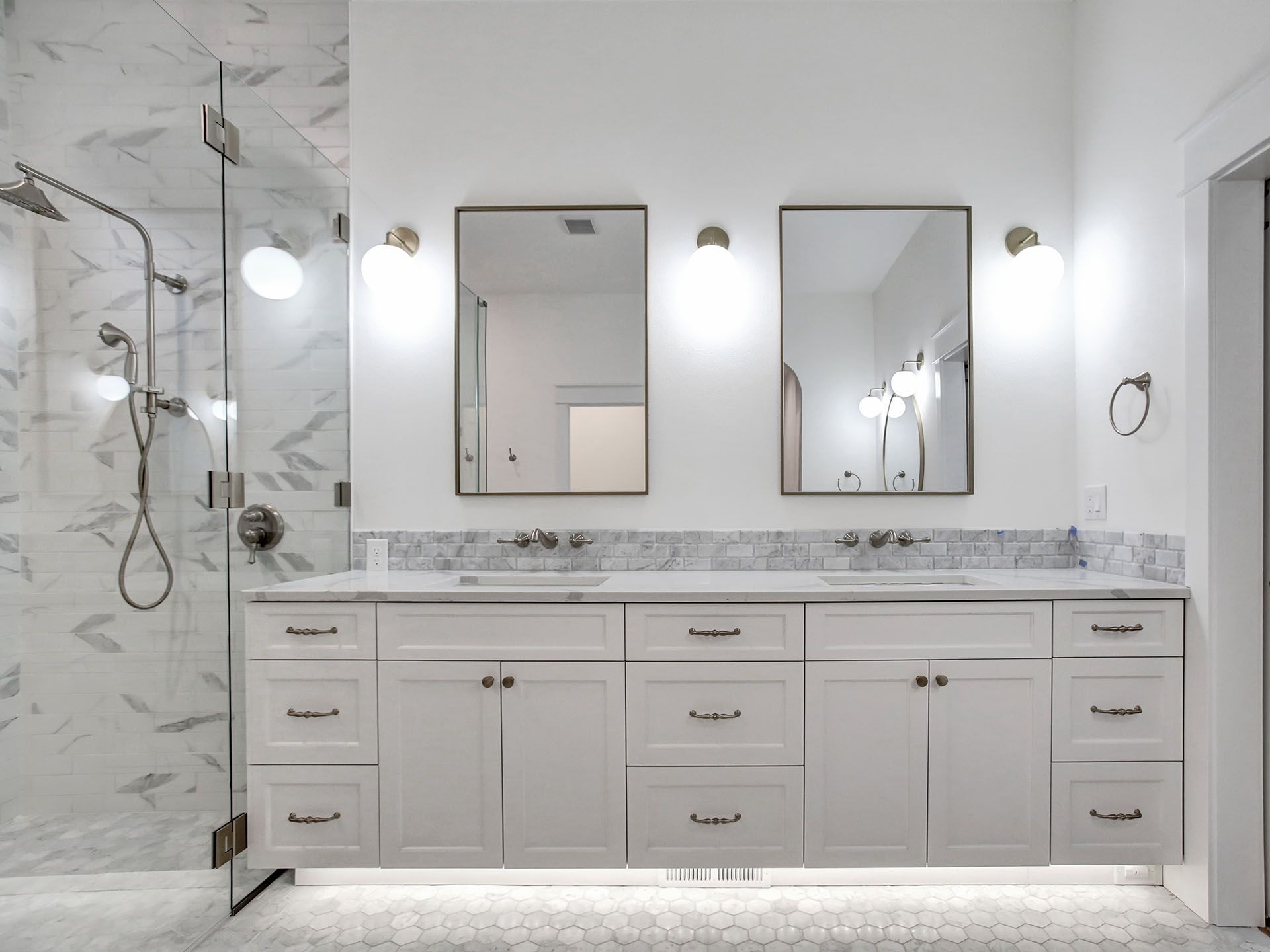 A bathroom with two sinks , two mirrors and a walk in shower.
