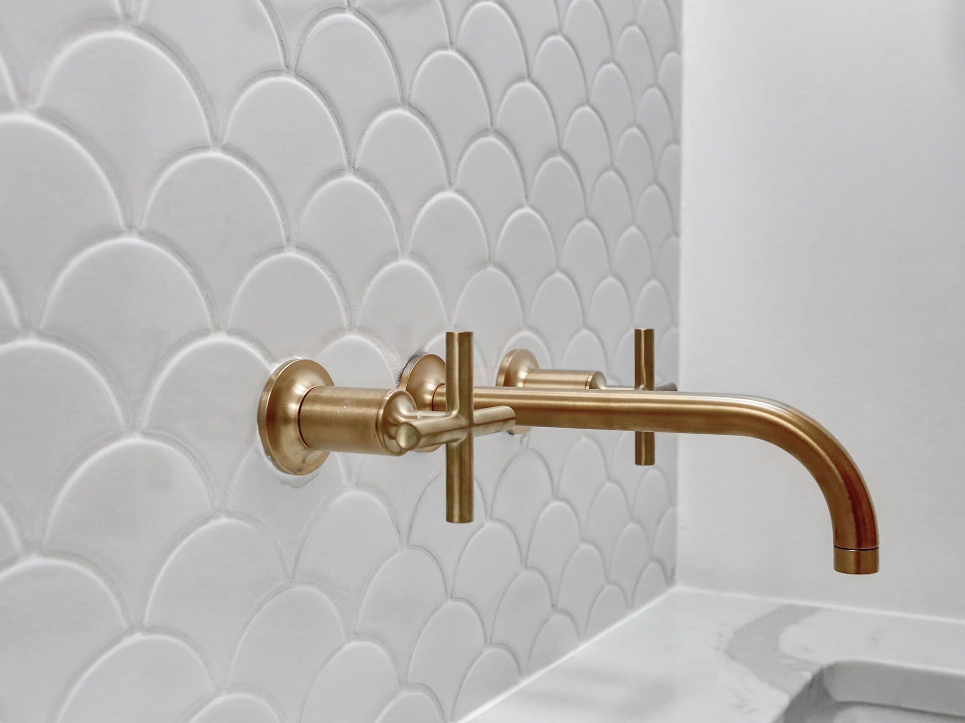 A bathroom sink with a brass faucet and a white tile wall.