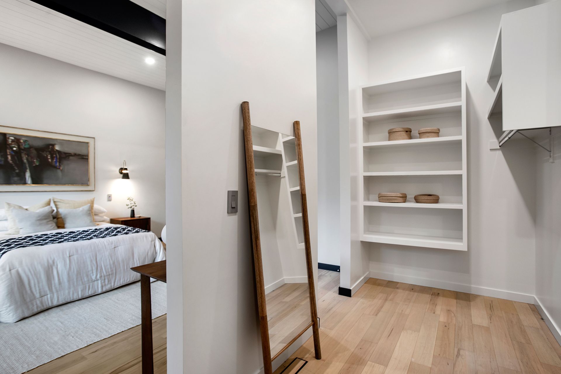 A bedroom with a bed, mirror, and open shelves