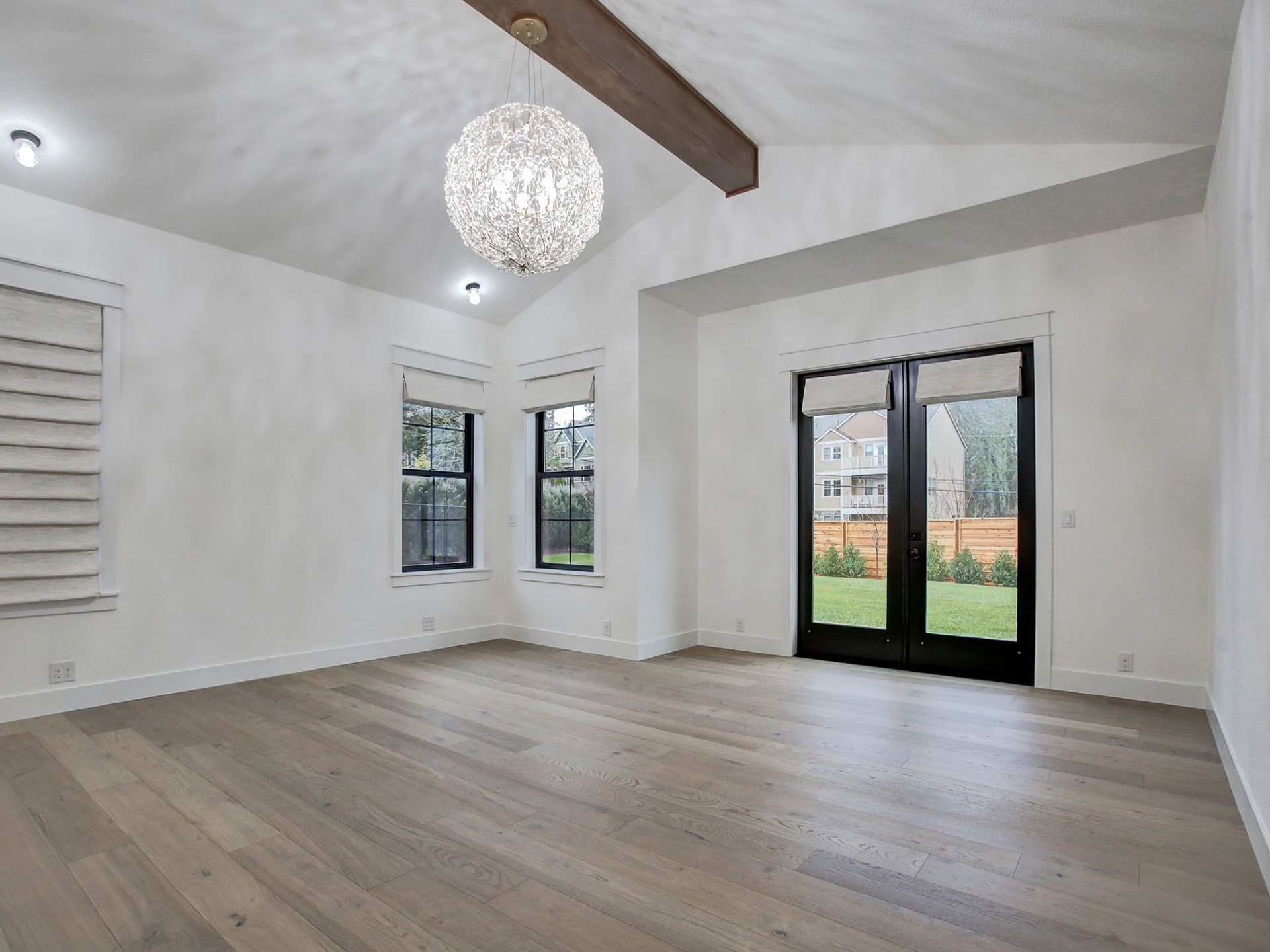 An empty living room with hardwood floors and a chandelier hanging from the ceiling