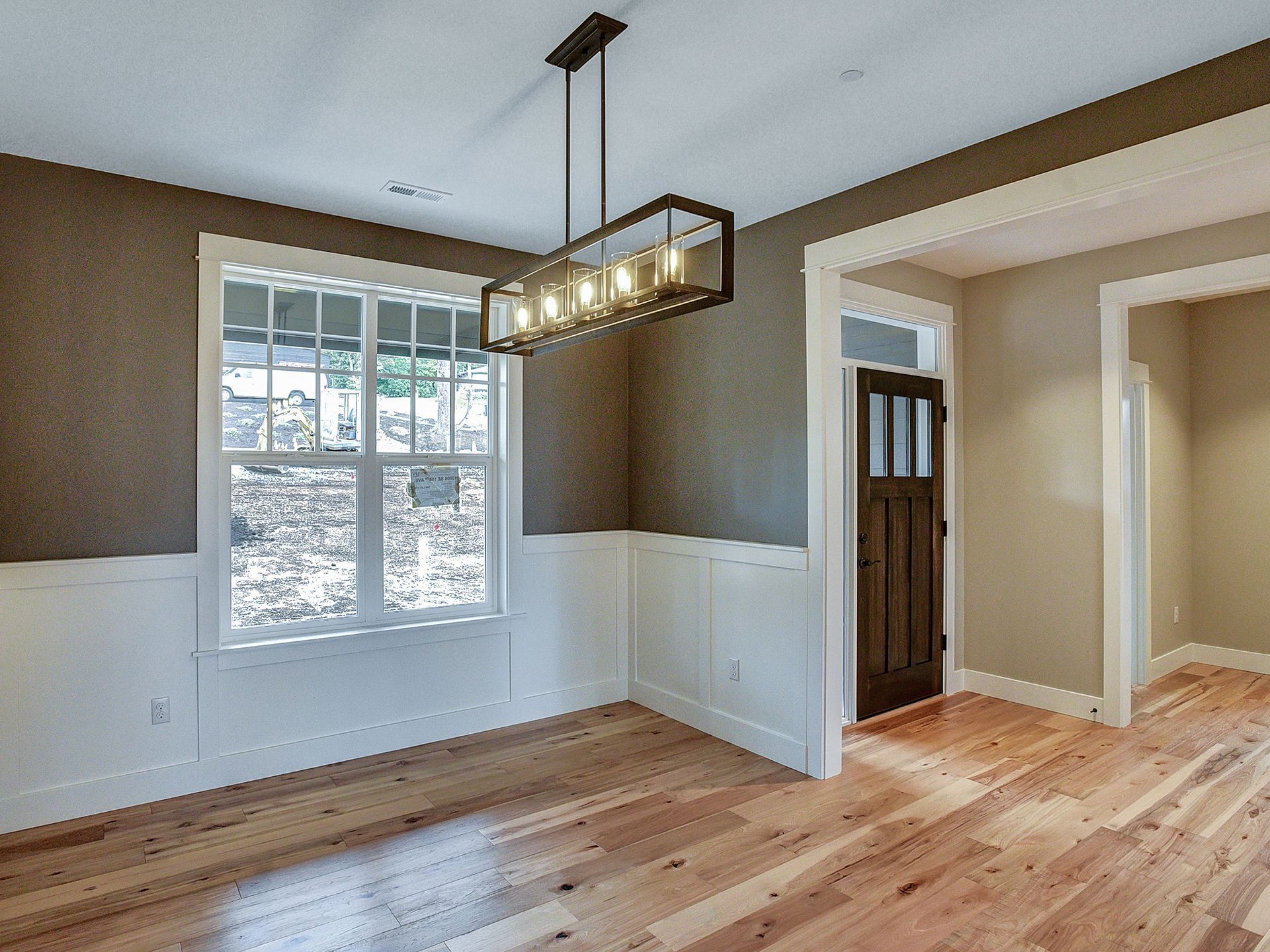 An empty room with hardwood floors and a chandelier hanging from the ceiling