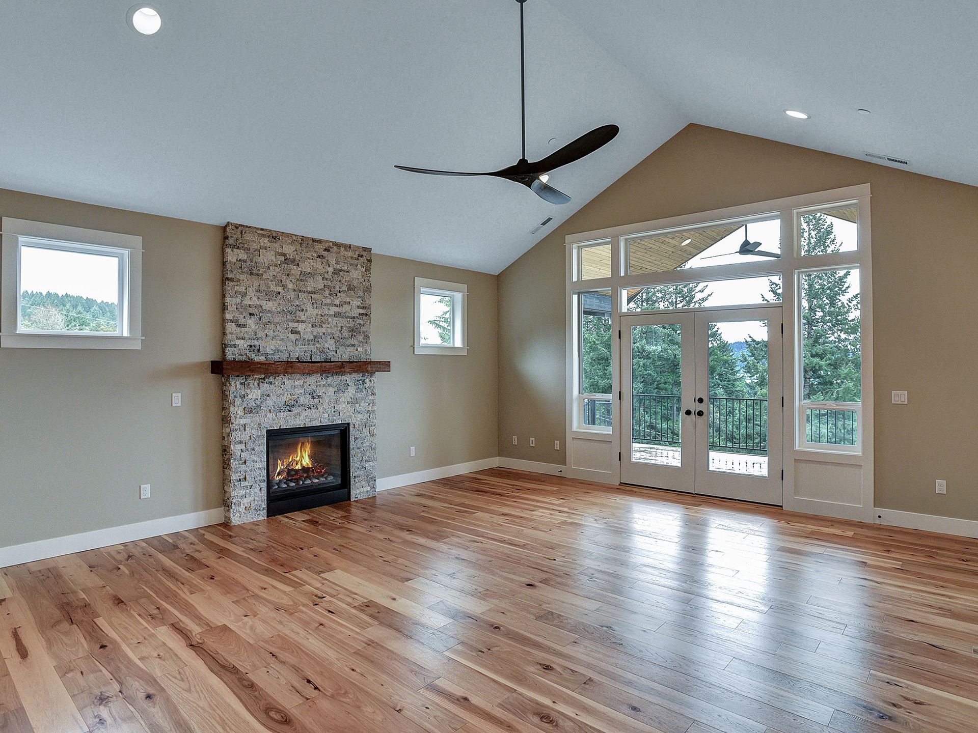 An empty living room with hardwood floors and a black ceiling fan