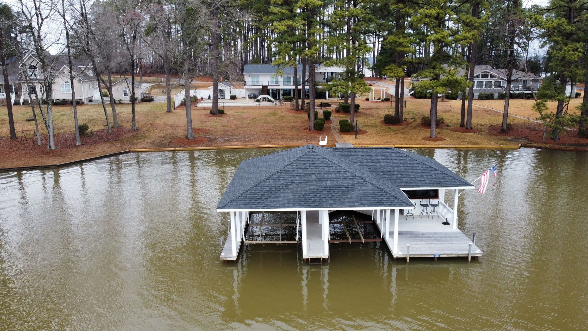 Flooded lakeside dock pavilion with a dark roof, surrounded by brown water and bare trees