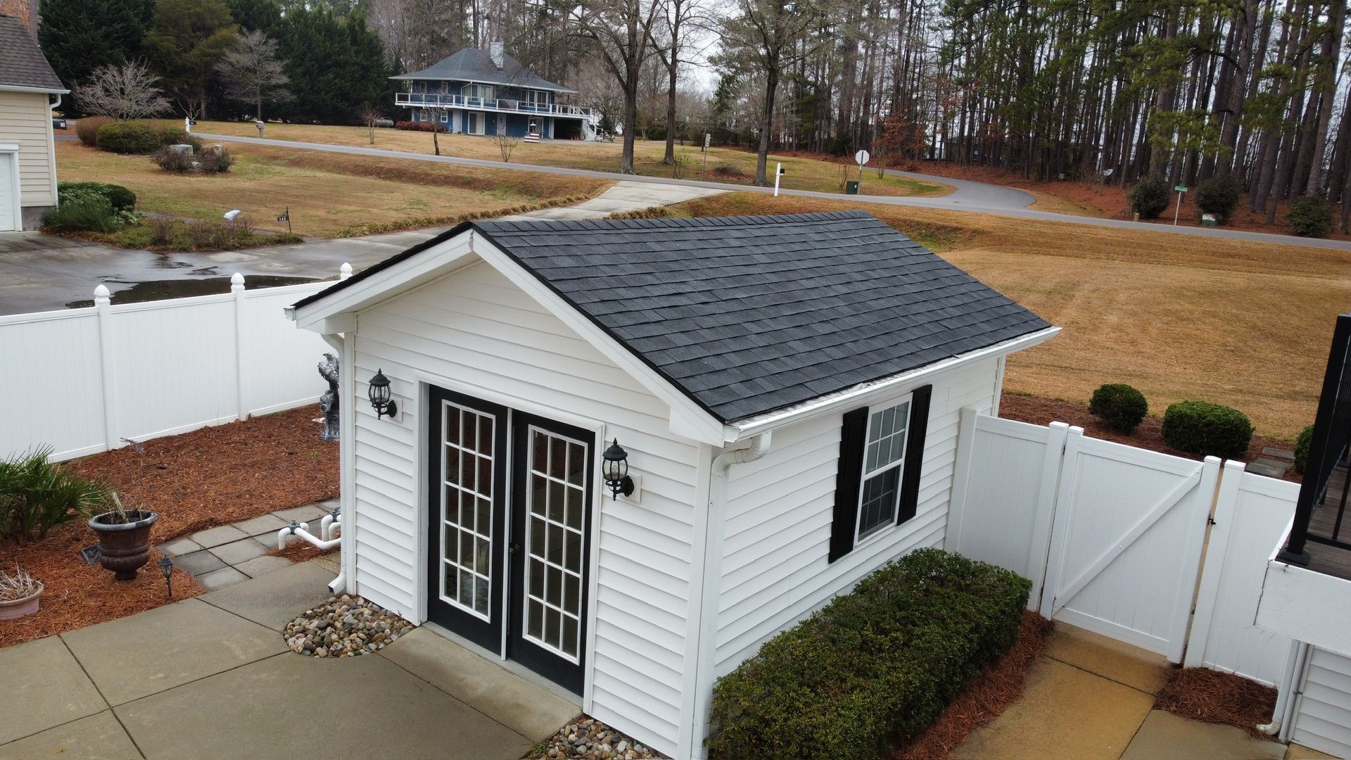 Small white backyard shed with dark roof, double doors, and fenced patio area