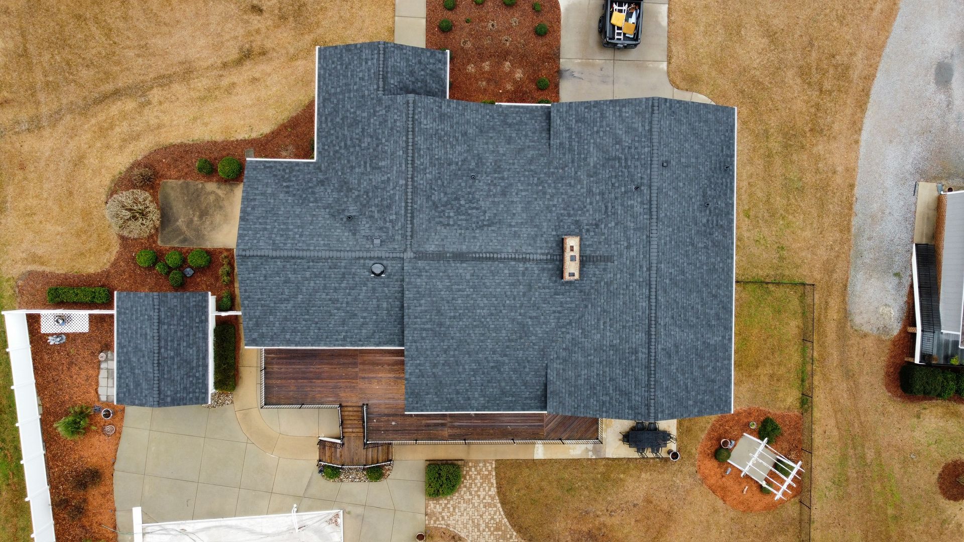 Aerial view of a house with a dark gray roof, surrounded by brown yard and small trees.