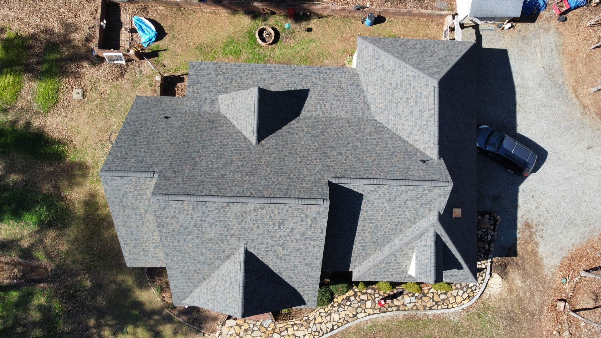 Aerial view of a gray shingled house roof with multiple gables and a small yard around it