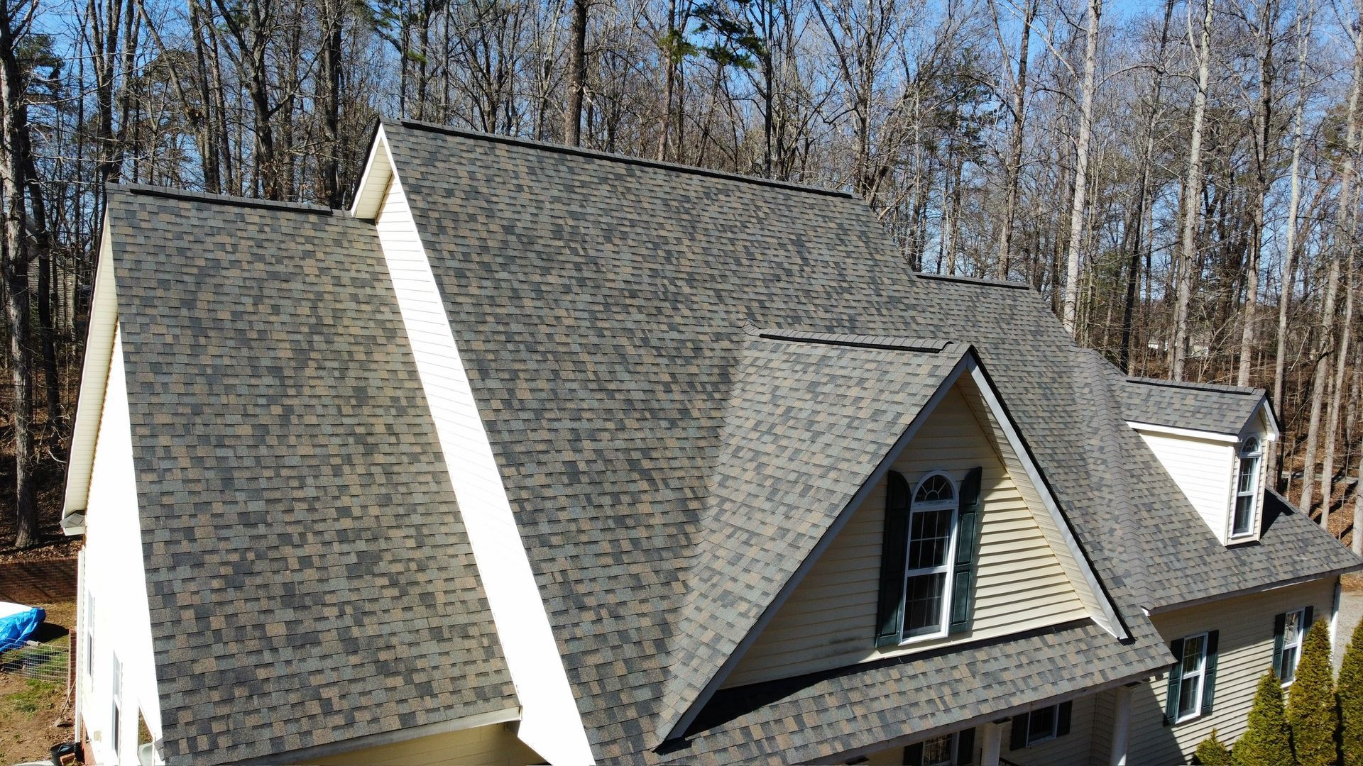 Gray-shingled house roof with steep gables and dormer windows in a wooded setting