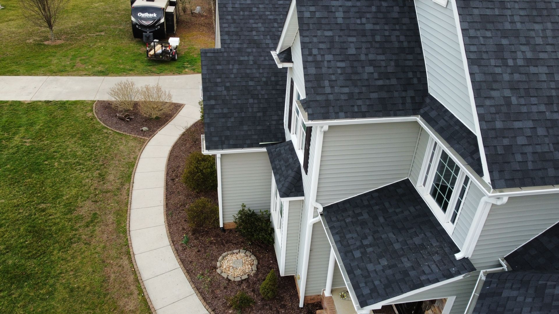Aerial view of a house with dark roof, curved walkway, lawn, and a black utility vehicle by the street.