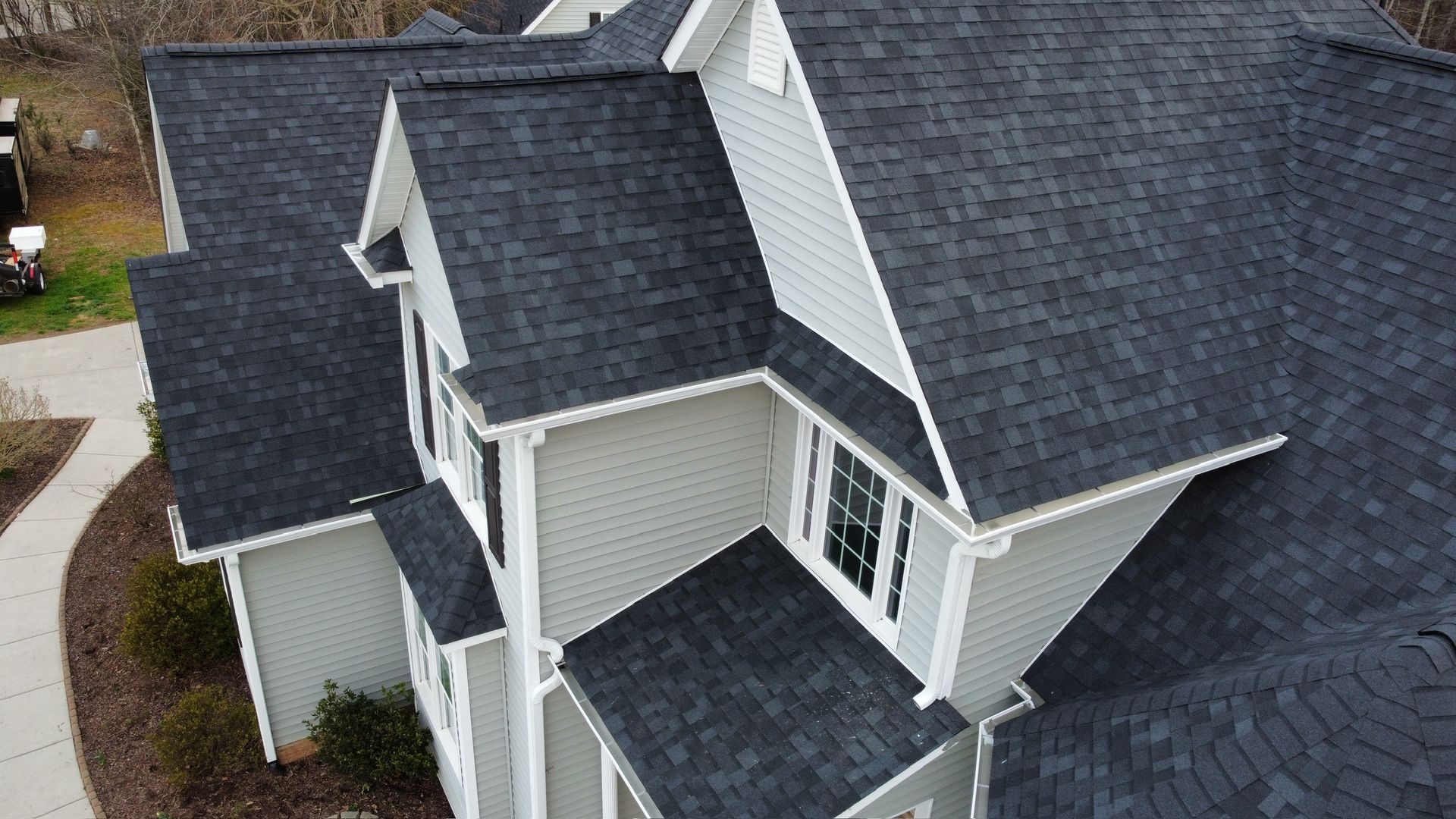 Aerial view of a gray shingled house roof with multiple dormers and white trim.