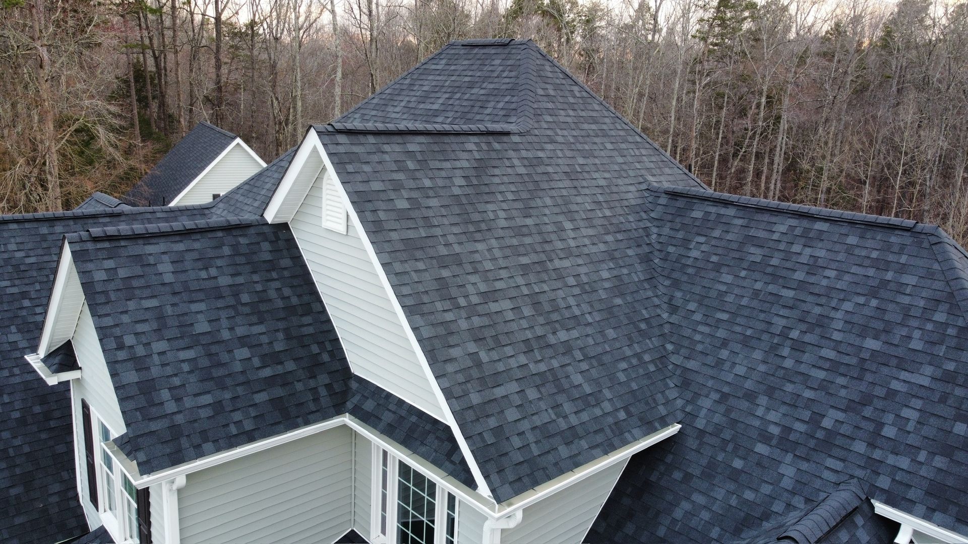 Gray-shingled roof on a house with dormers, viewed from above with wooded trees in the background