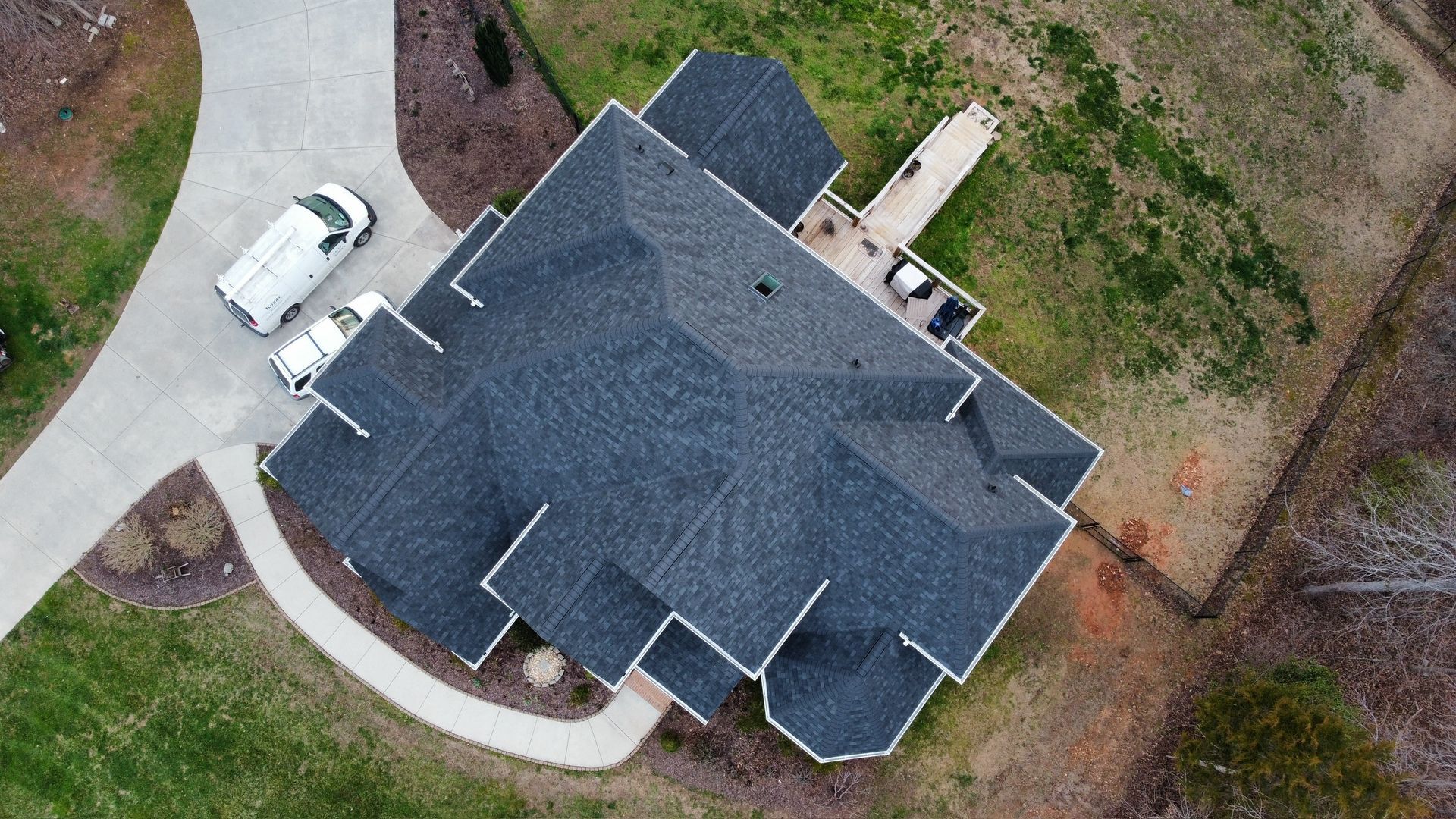 Aerial view of a house with a dark roof and a white van parked beside it.