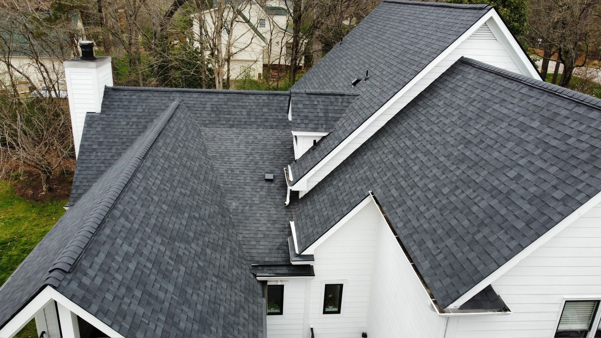 Gray shingled roof with multiple slopes and white siding on a house, viewed from above