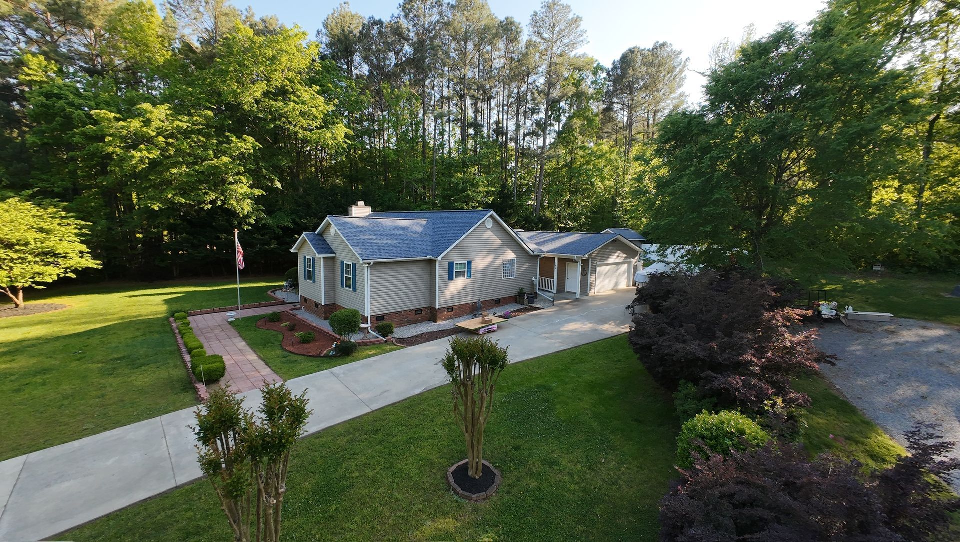 Suburban house with blue roof and brick walkway, surrounded by a green lawn and trees.