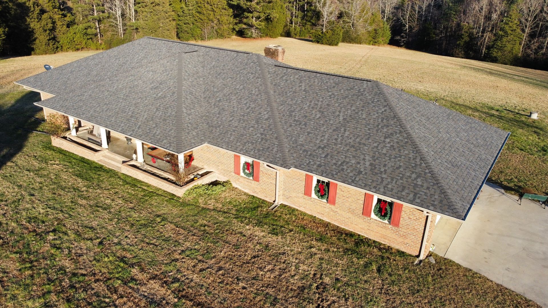 Aerial view of a single-story beige house with a dark gray roof and red shutters in a rural setting