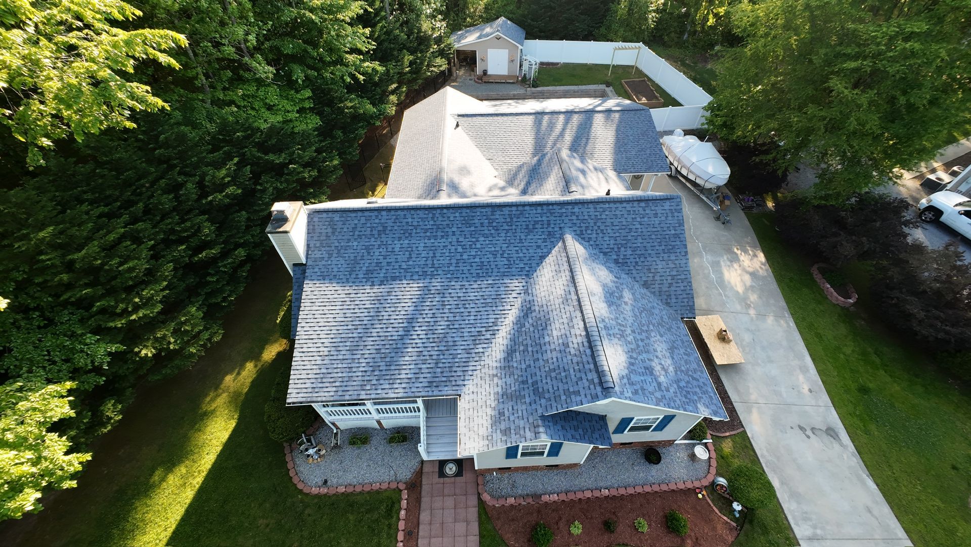 Aerial view of a blue-gray house with a driveway, brick walkway, and surrounding trees