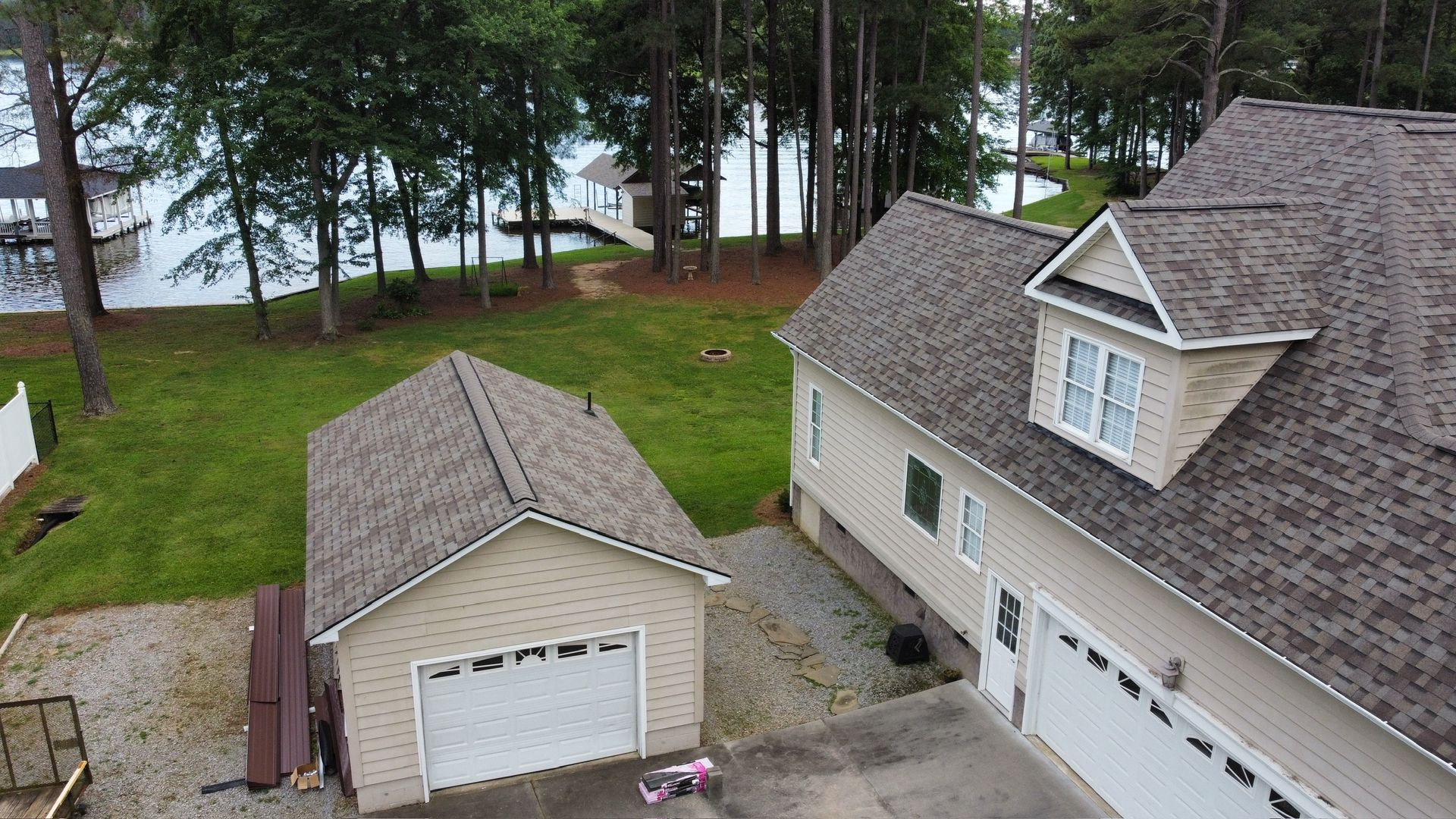 Aerial view of a house, detached garage, and driveway beside a wooded lakeside yard