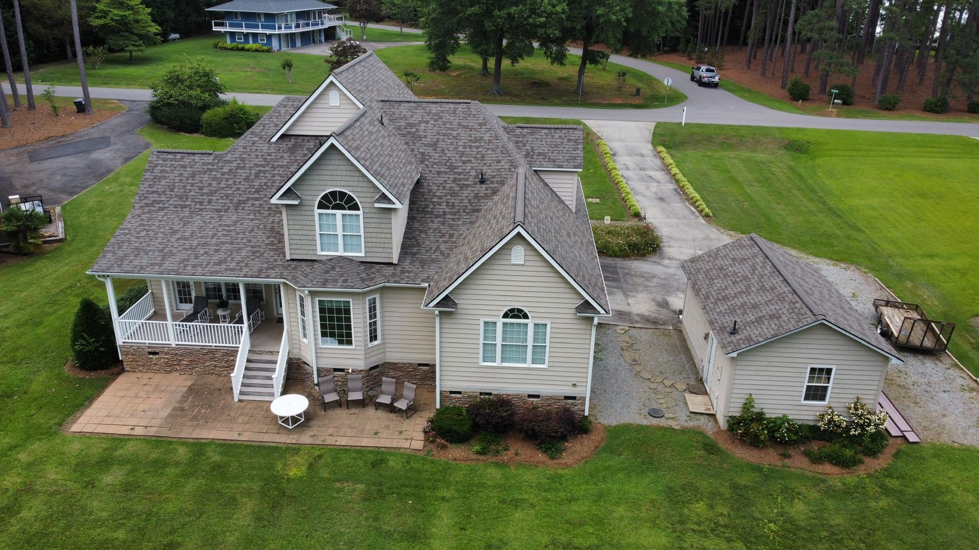 Aerial view of a beige suburban house with a gray roof and a large green lawn.