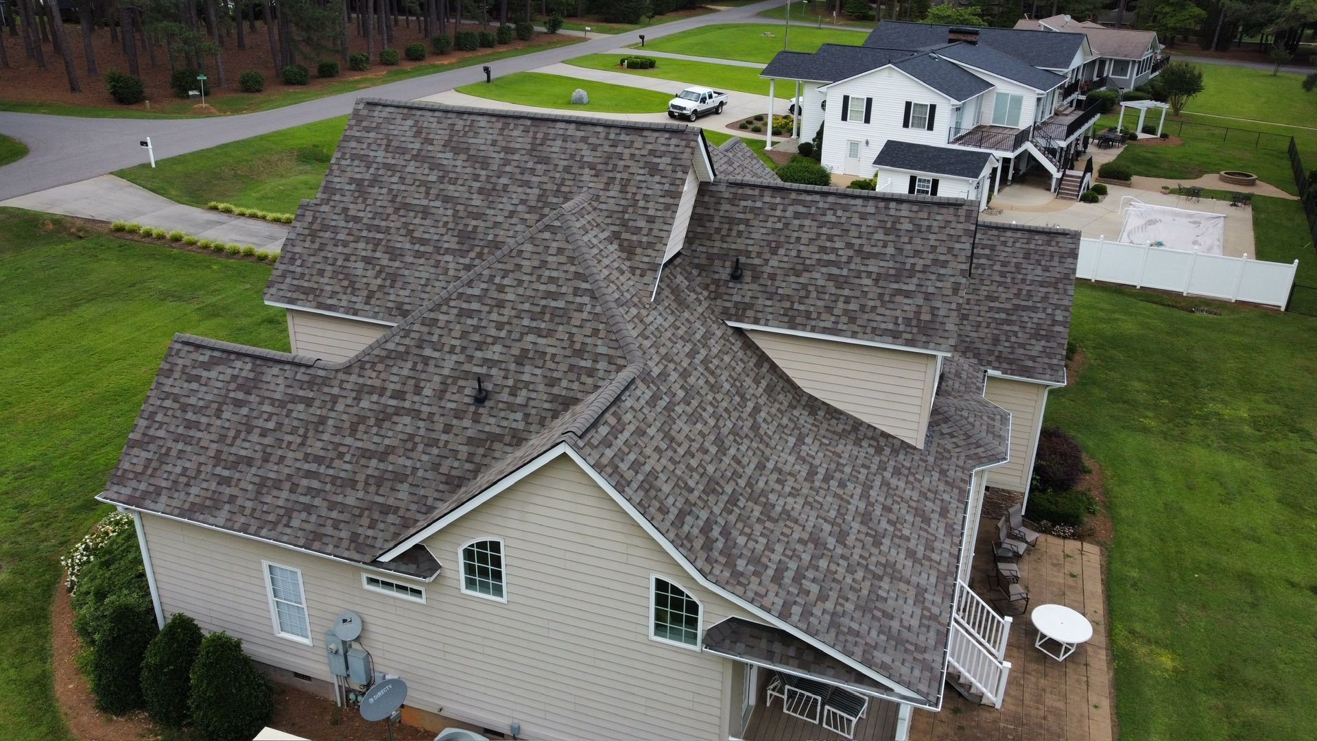 Aerial view of a house roof with gray shingles and beige siding in a suburban neighborhood