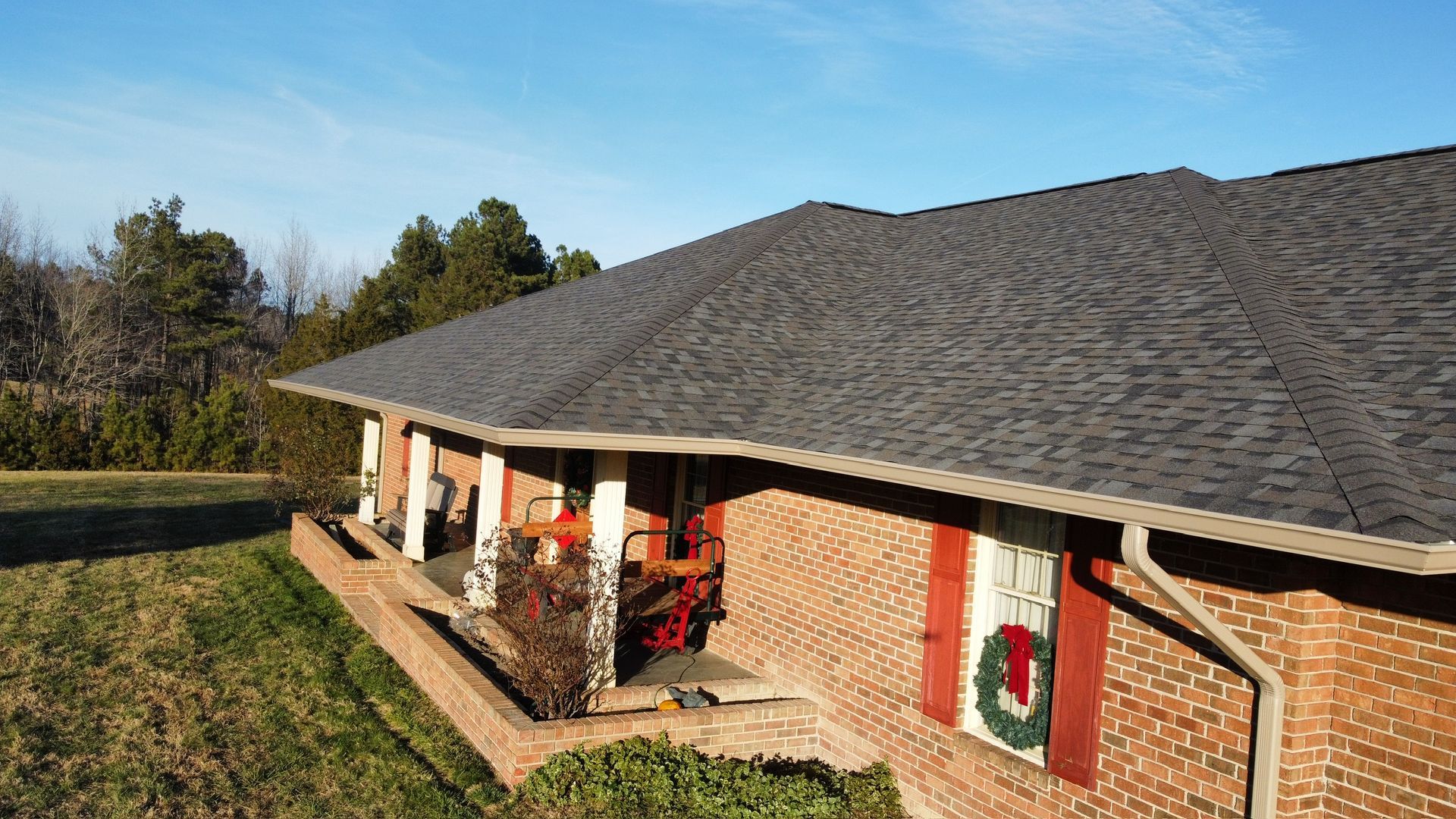 Brick house with a covered porch, red front door, and a shingled roof in a grassy yard.