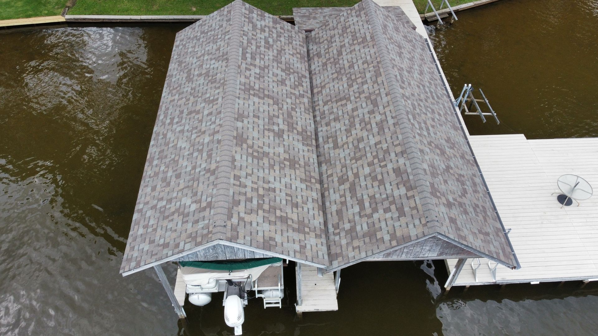 Aerial view of a covered dock beside brown water, with a small white boat moored underneath.