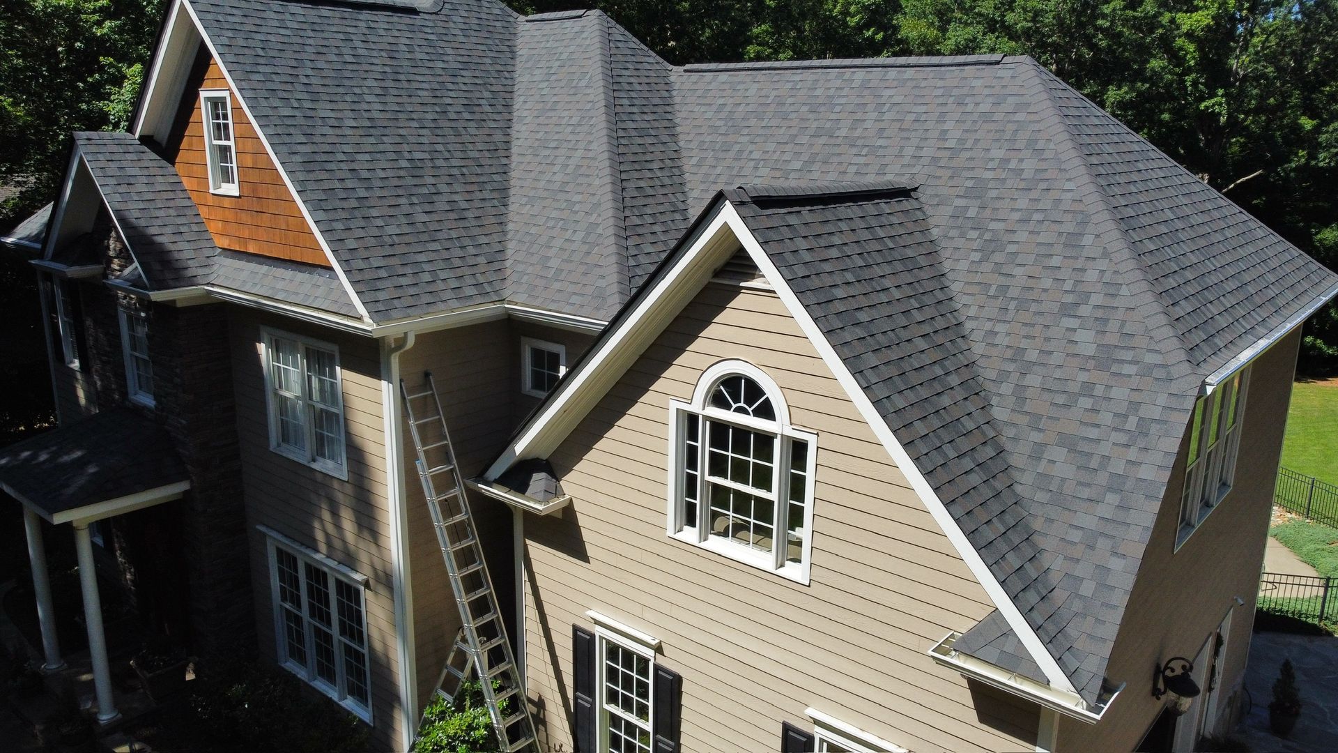 Aerial view of a beige house with a gray shingled roof and dormer windows.