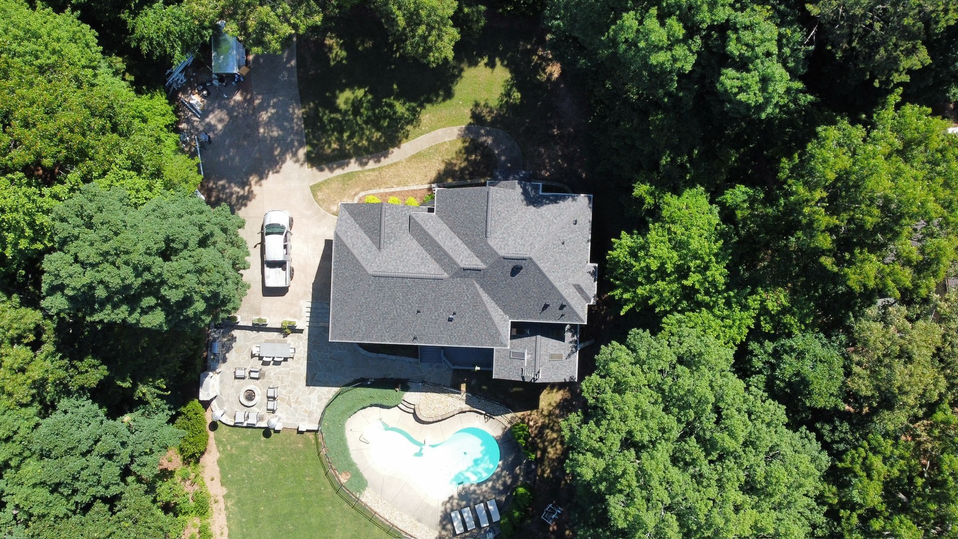 Aerial view of a house with a backyard pool surrounded by dense green trees