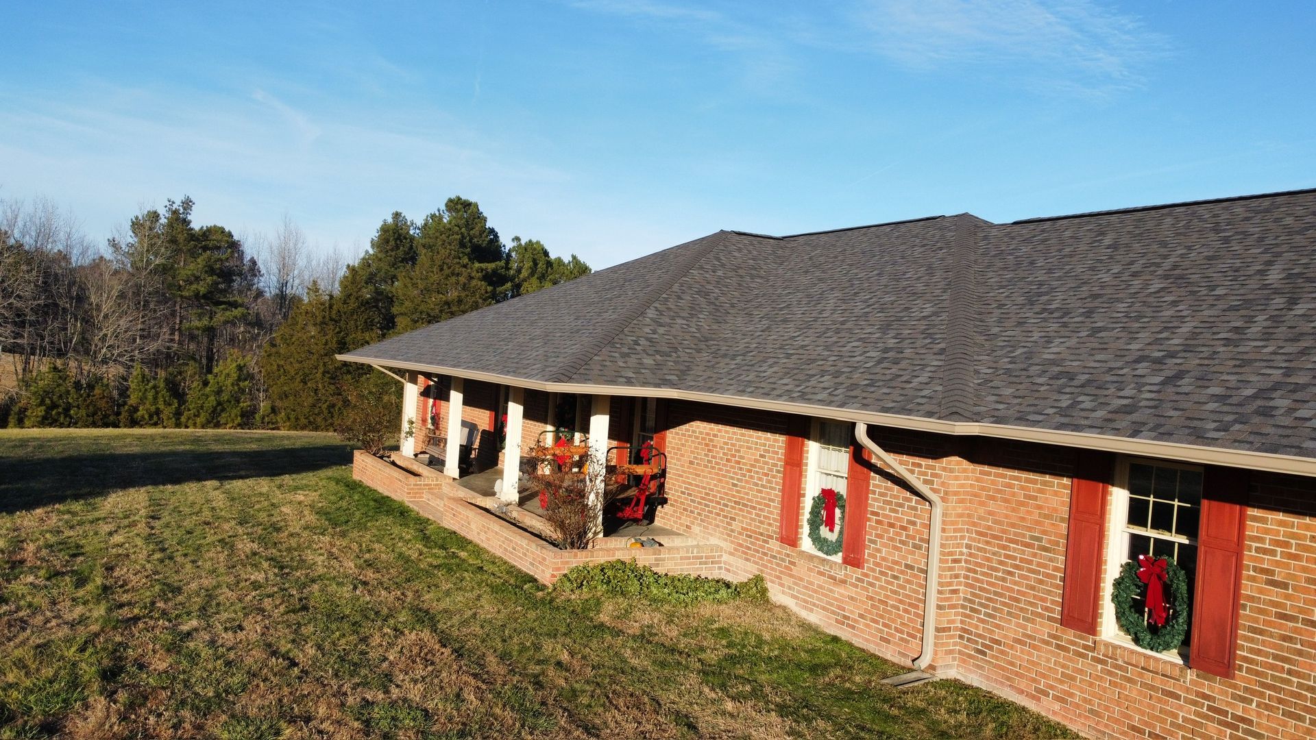 Brick ranch house with a dark roof, red holiday wreaths, and a grassy yard in daylight