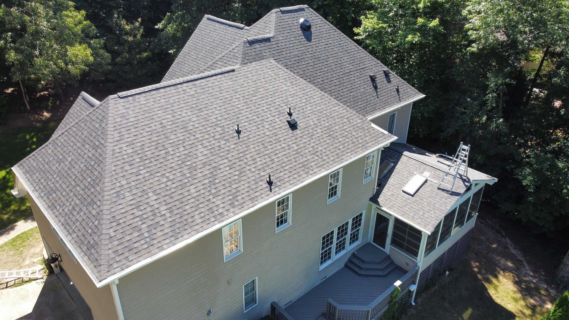 Aerial view of a gray house with a dark roof and screened porch surrounded by trees.