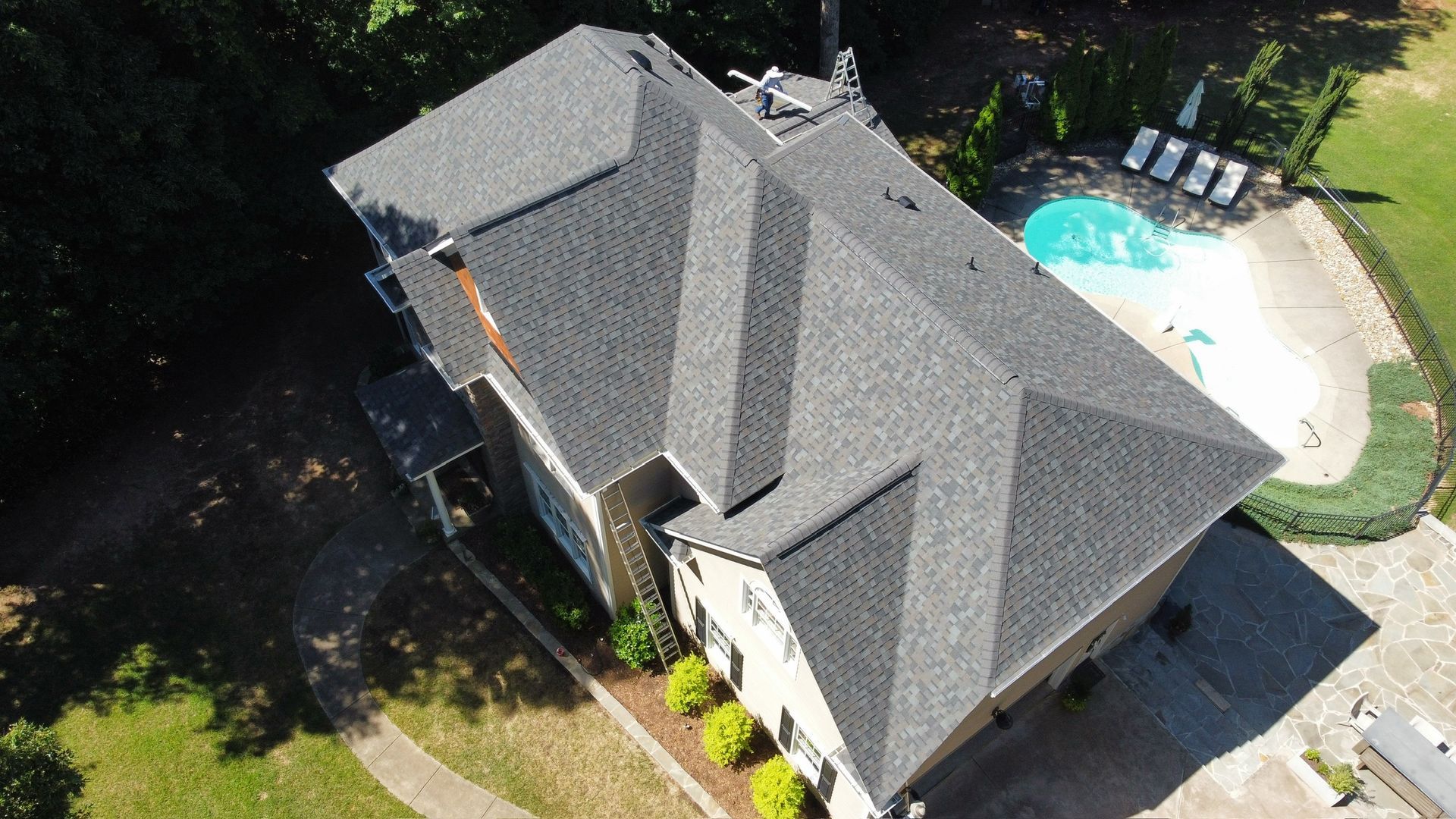 Aerial view of a gray-roofed house with a backyard pool and patio.