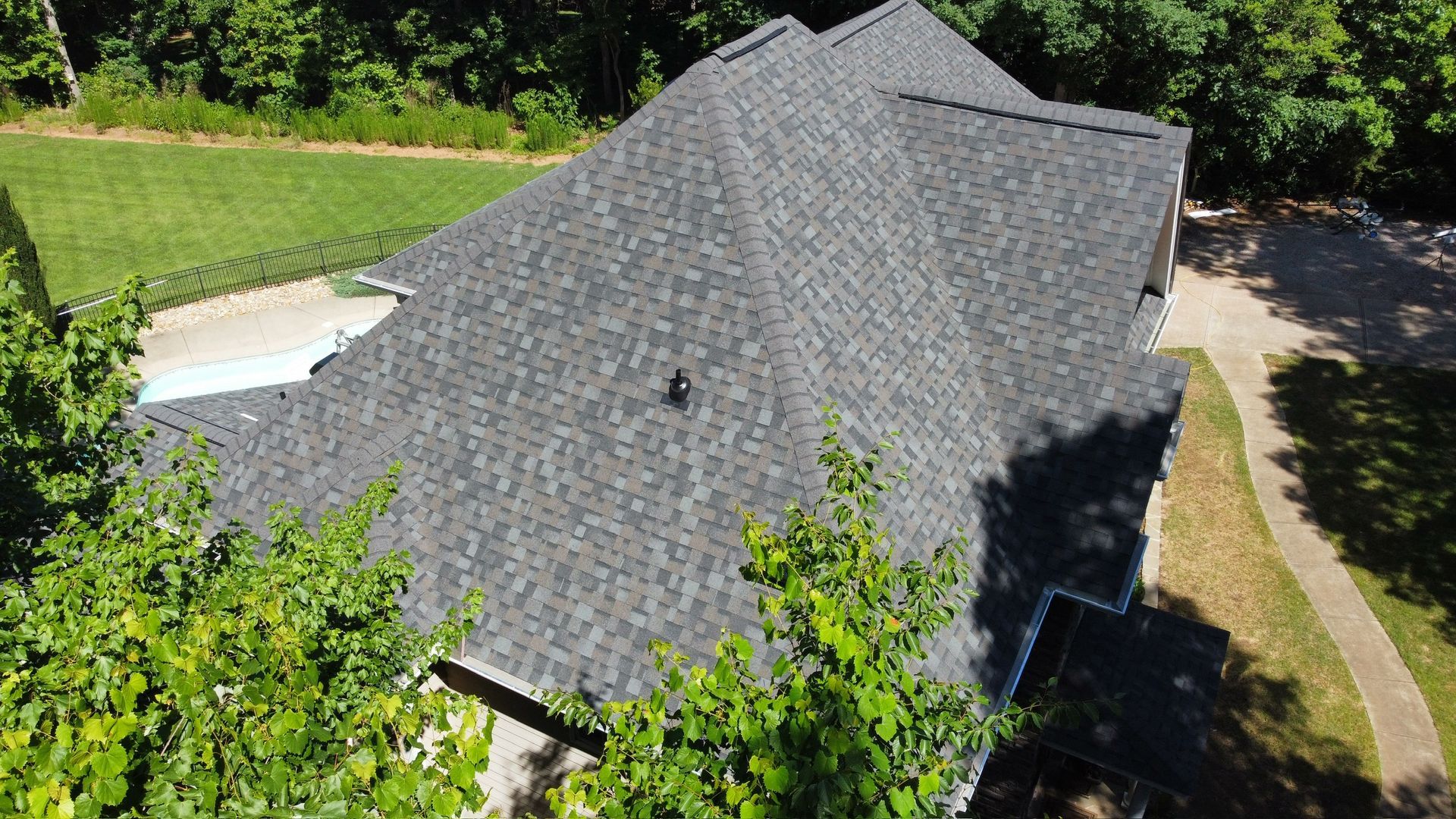 Aerial view of a gray shingled house roof surrounded by trees and a driveway