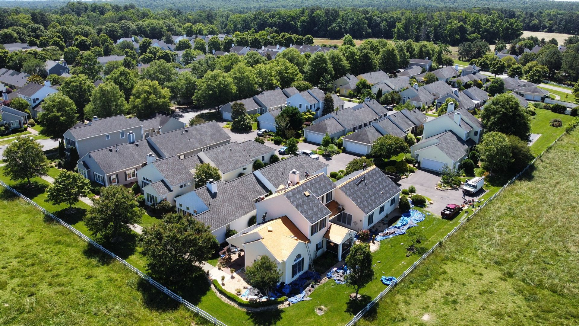 Aerial view of a suburban housing complex with gray roofs, green lawns, and surrounding trees.