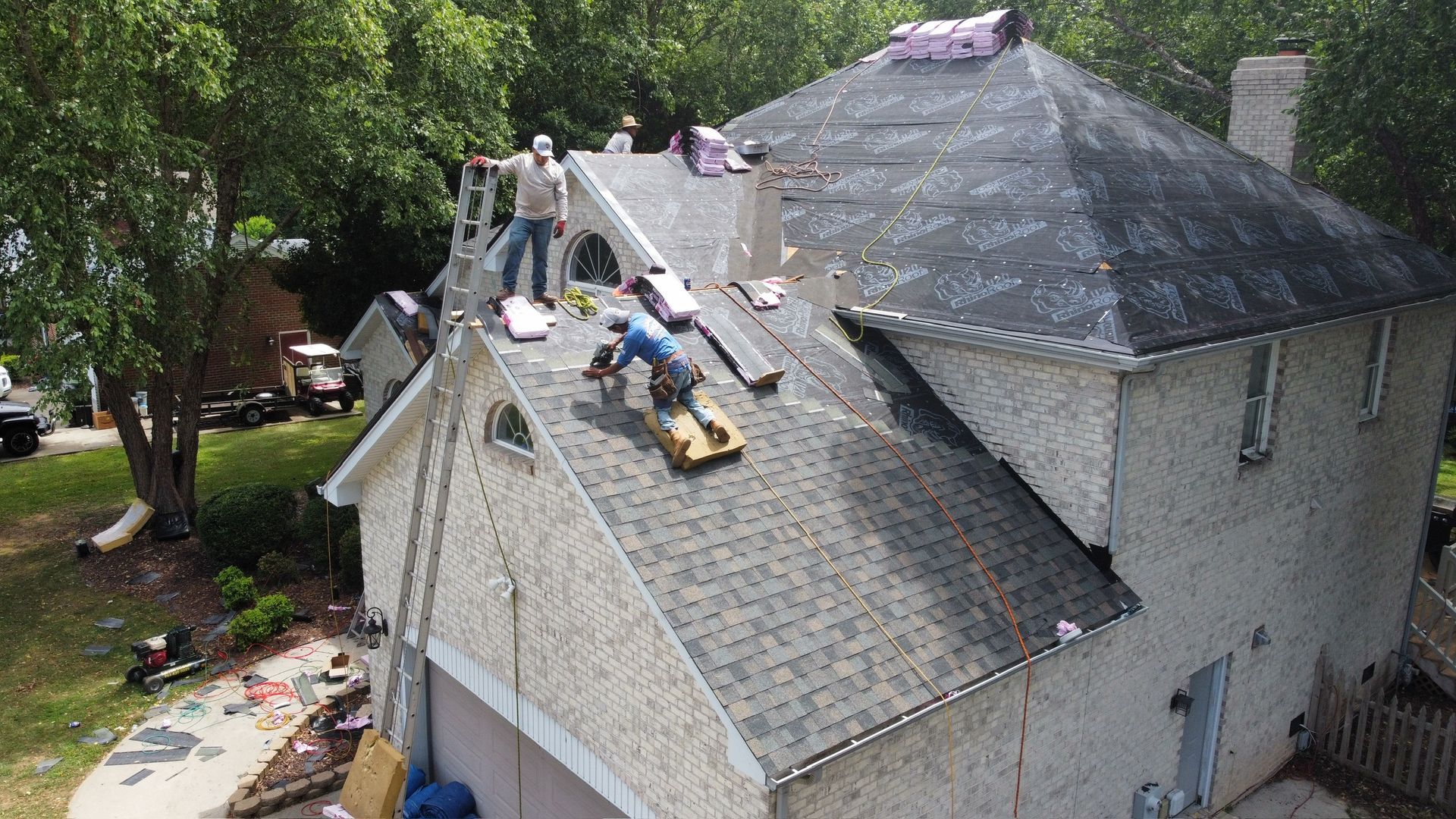 Roofers working on a gray shingled house roof beside a dark dormer