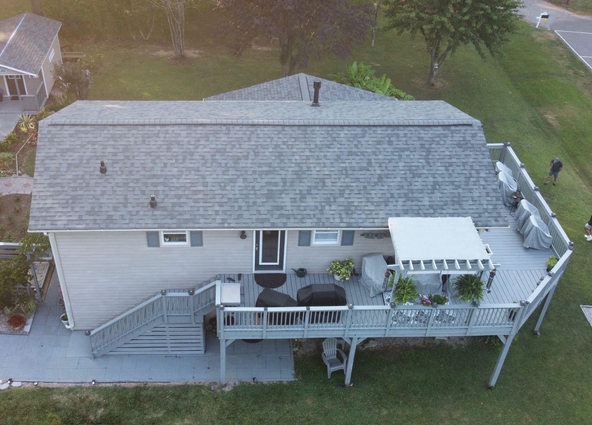Aerial view of a gray house with a front deck, stairs, and white awning in a grassy yard.