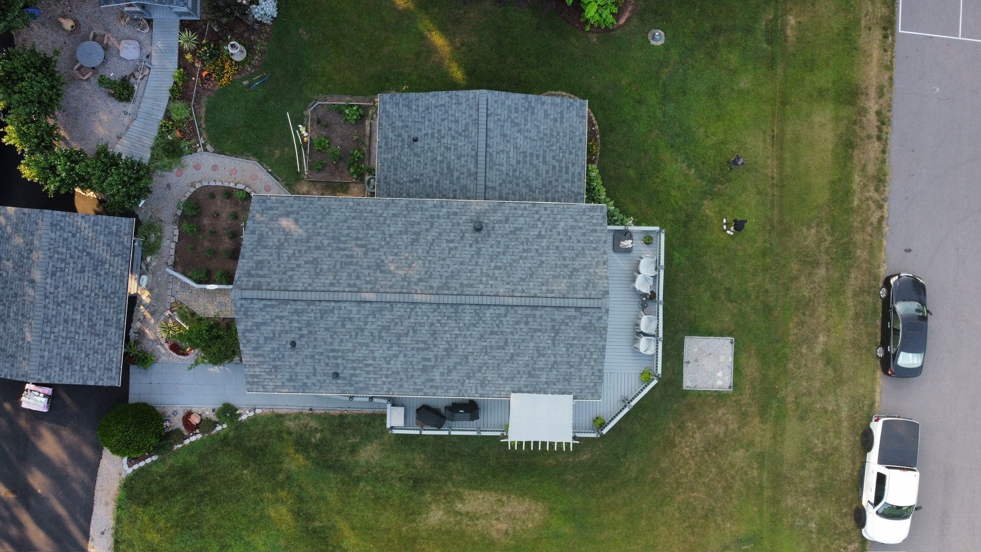 Aerial view of a house with gray roof, lawn, driveway, and two parked cars.