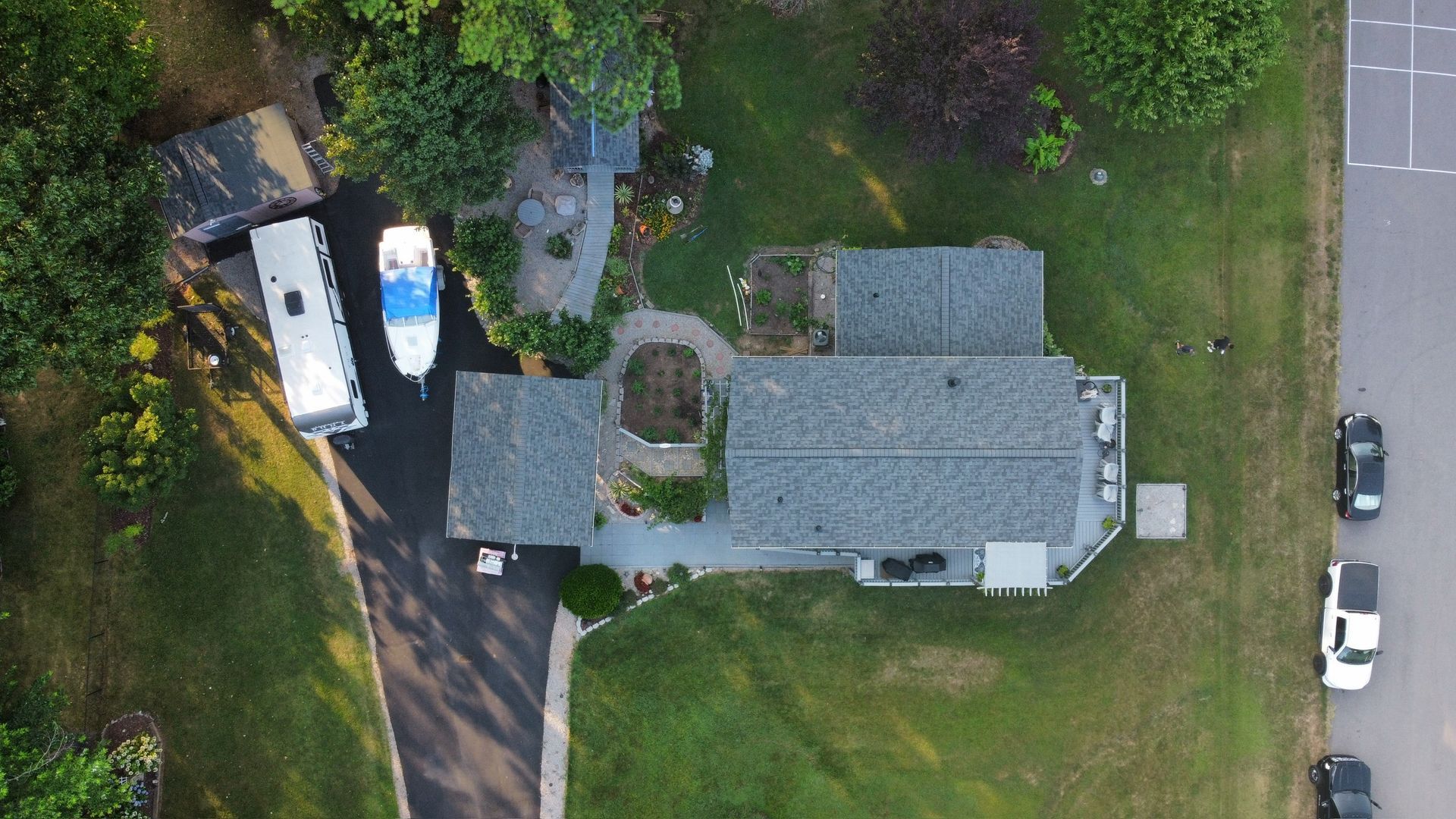 Aerial view of a house with parked vehicles beside a driveway and a grassy yard along a road.