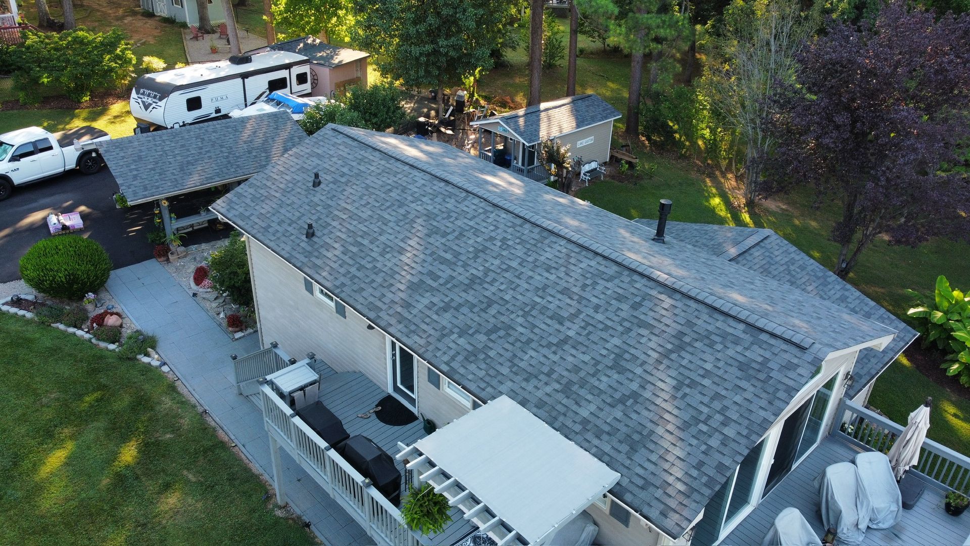 Aerial view of a gray-roofed house with a patio, surrounded by trees and parked vehicles.